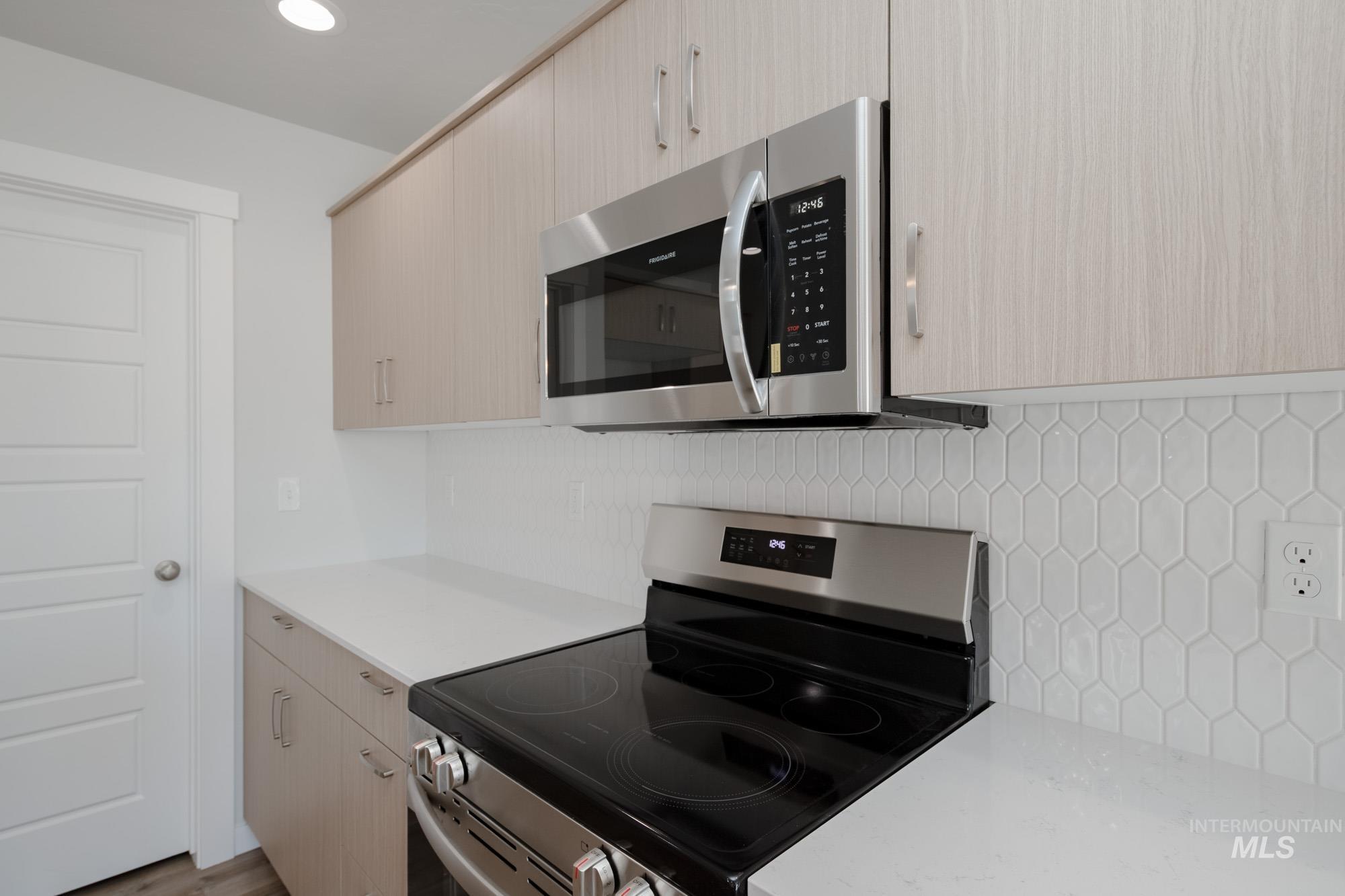Kitchen featuring stainless steel appliances, decorative backsplash, light stone counters, modern cabinets, and light brown cabinetry