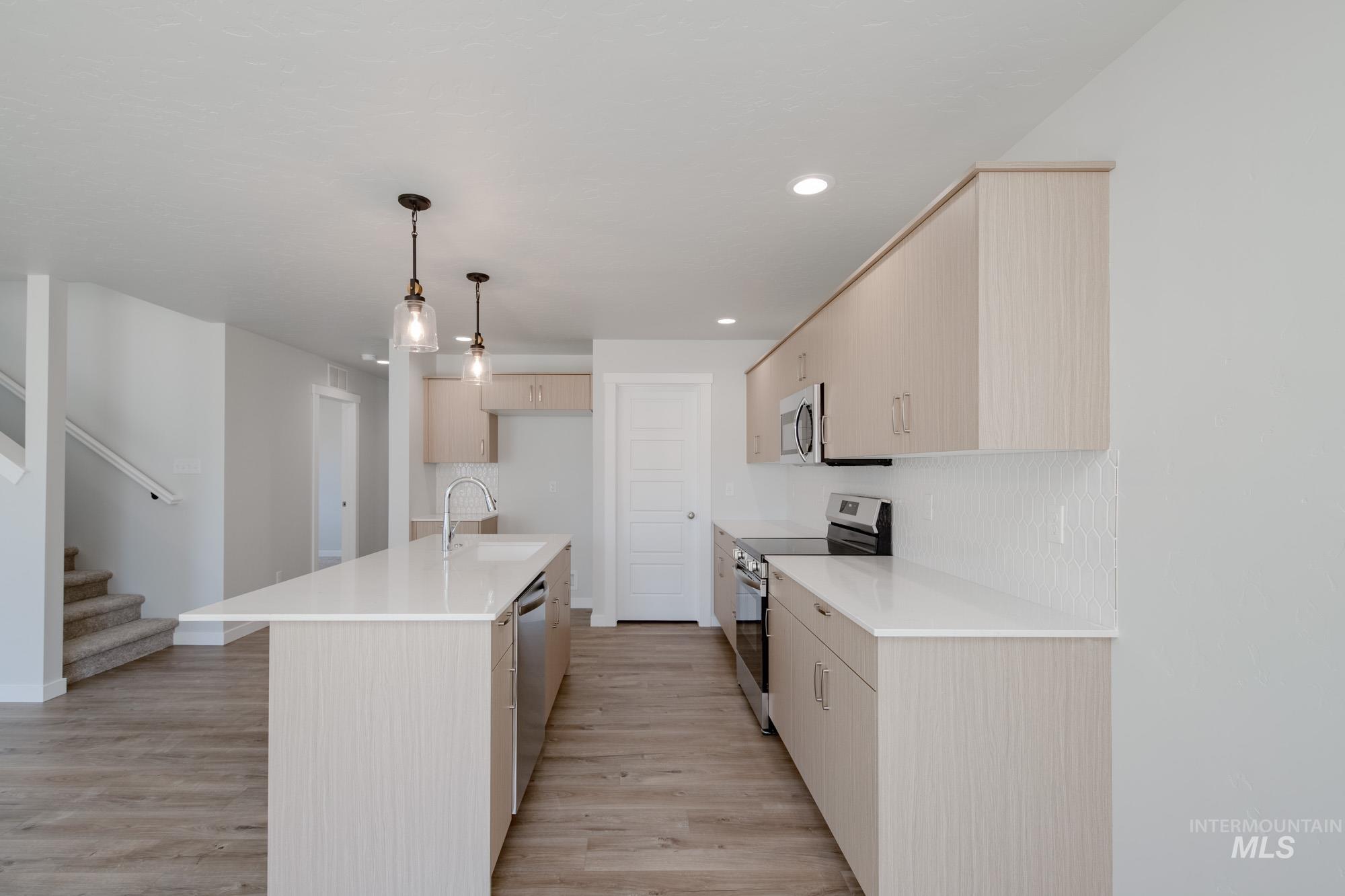 Kitchen with appliances with stainless steel finishes, a center island with sink, recessed lighting, light wood finished floors, and hanging light fixtures