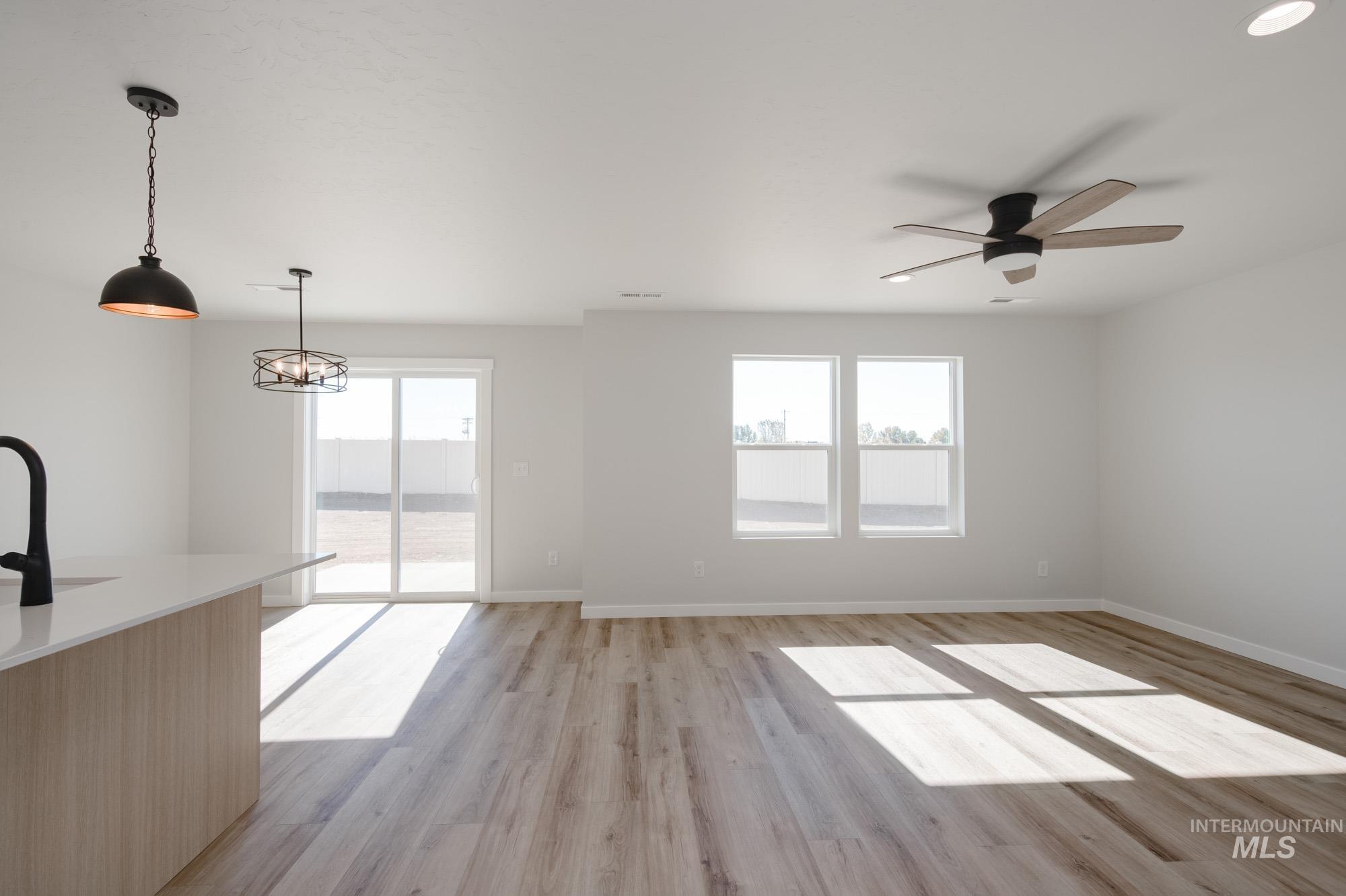 Unfurnished living room with plenty of natural light, light wood finished floors, ceiling fan, and a chandelier