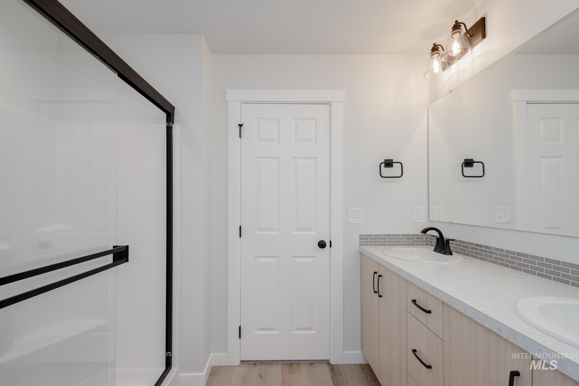 Bathroom with light wood finished floors, double vanity, and a shower stall