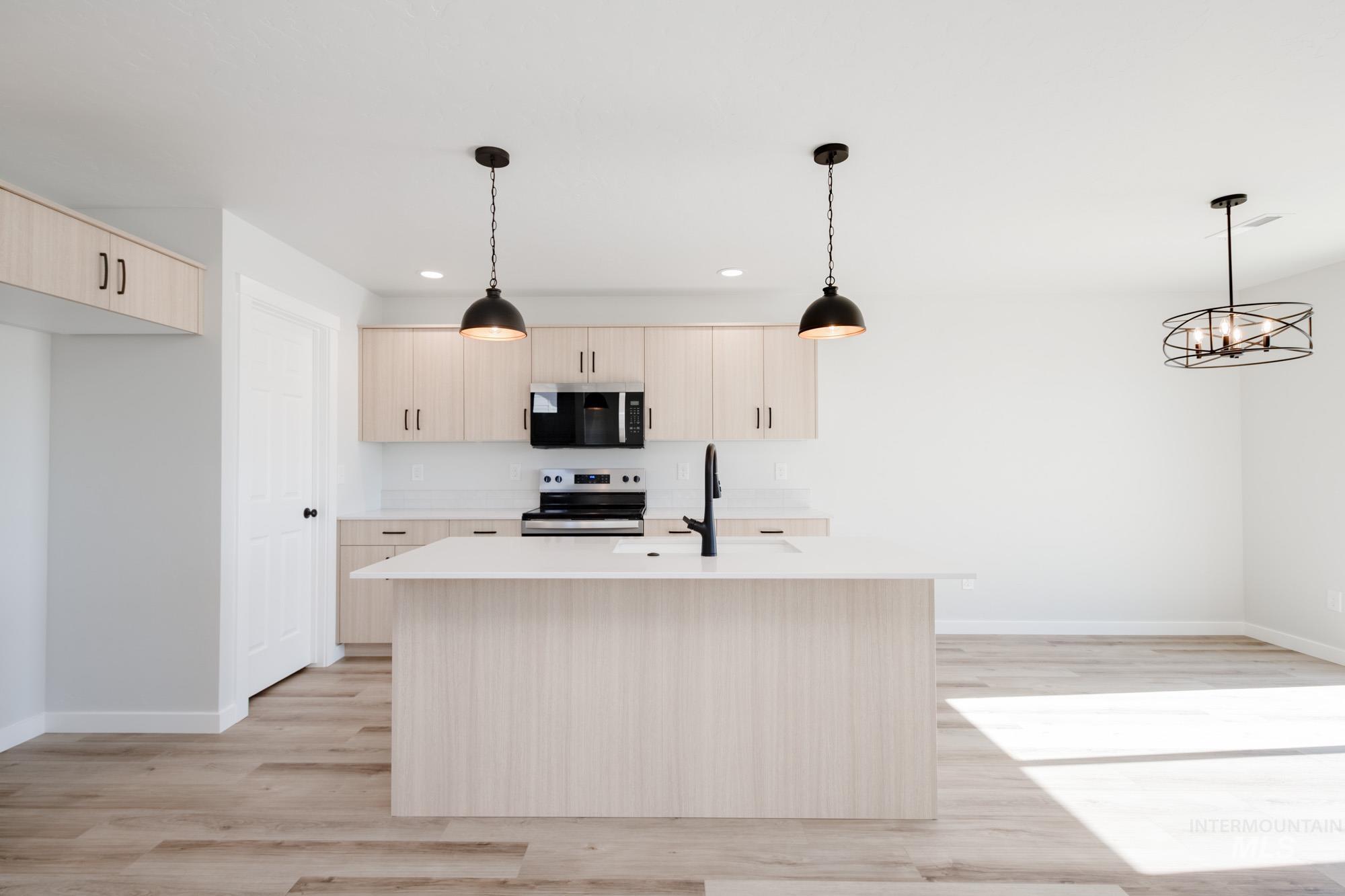 Kitchen featuring pendant lighting, light brown cabinets, black microwave, stainless steel electric range oven, and a kitchen island with sink