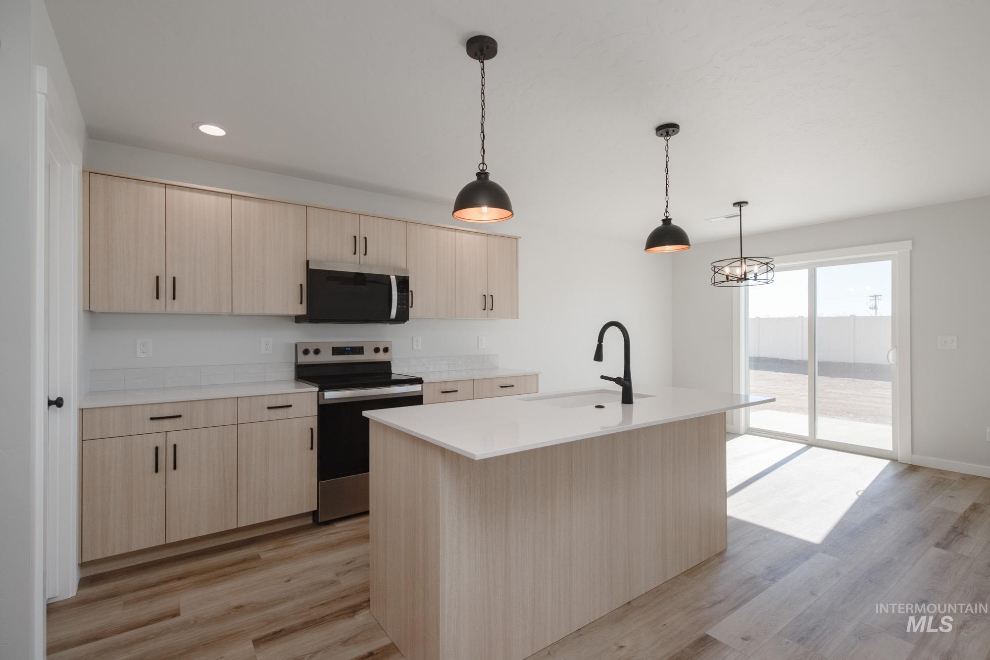 Kitchen featuring light brown cabinets, stainless steel appliances, decorative light fixtures, light wood finished floors, and recessed lighting