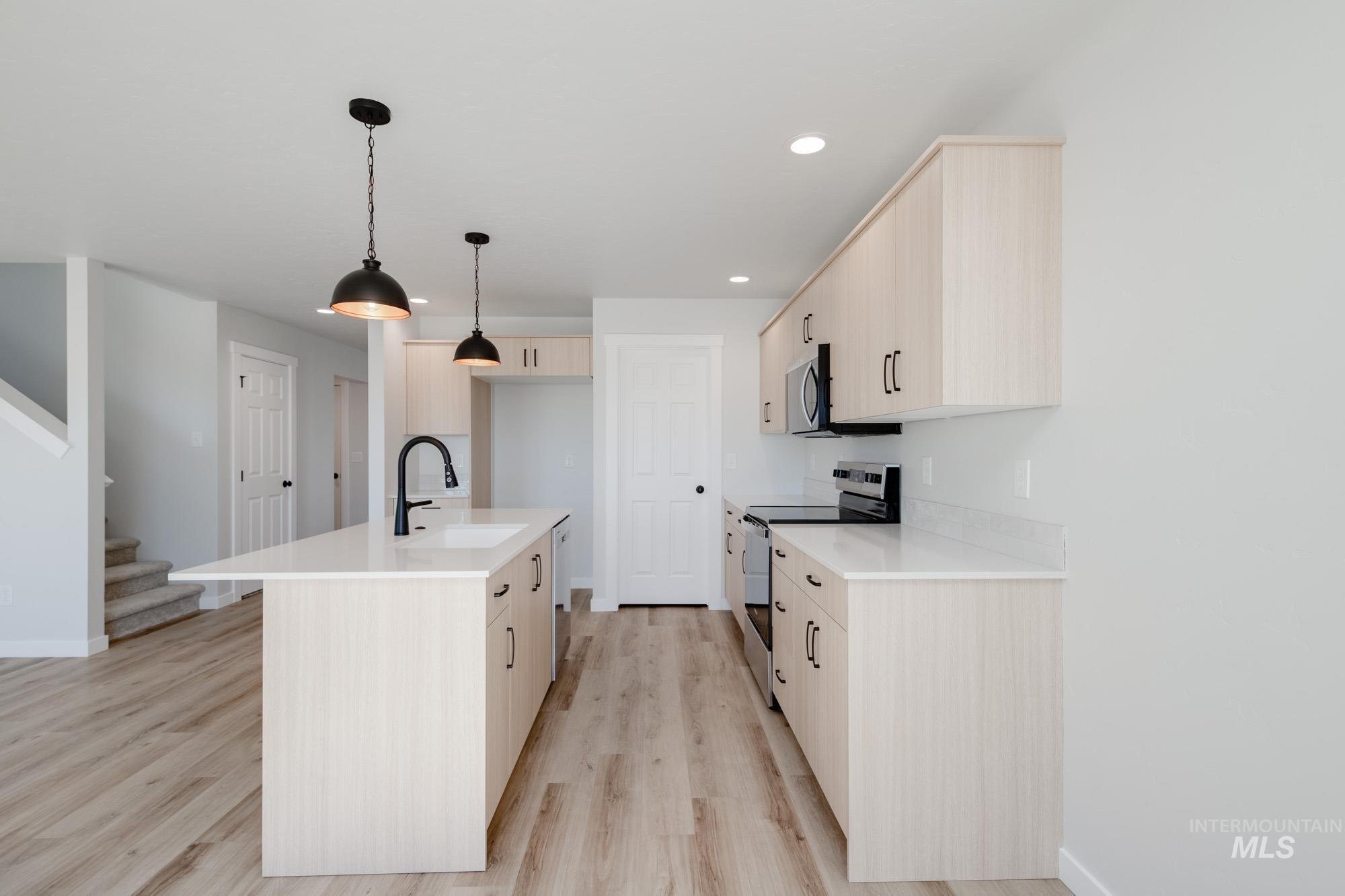 Kitchen with stainless steel appliances, a kitchen island with sink, light wood-type flooring, hanging light fixtures, and recessed lighting