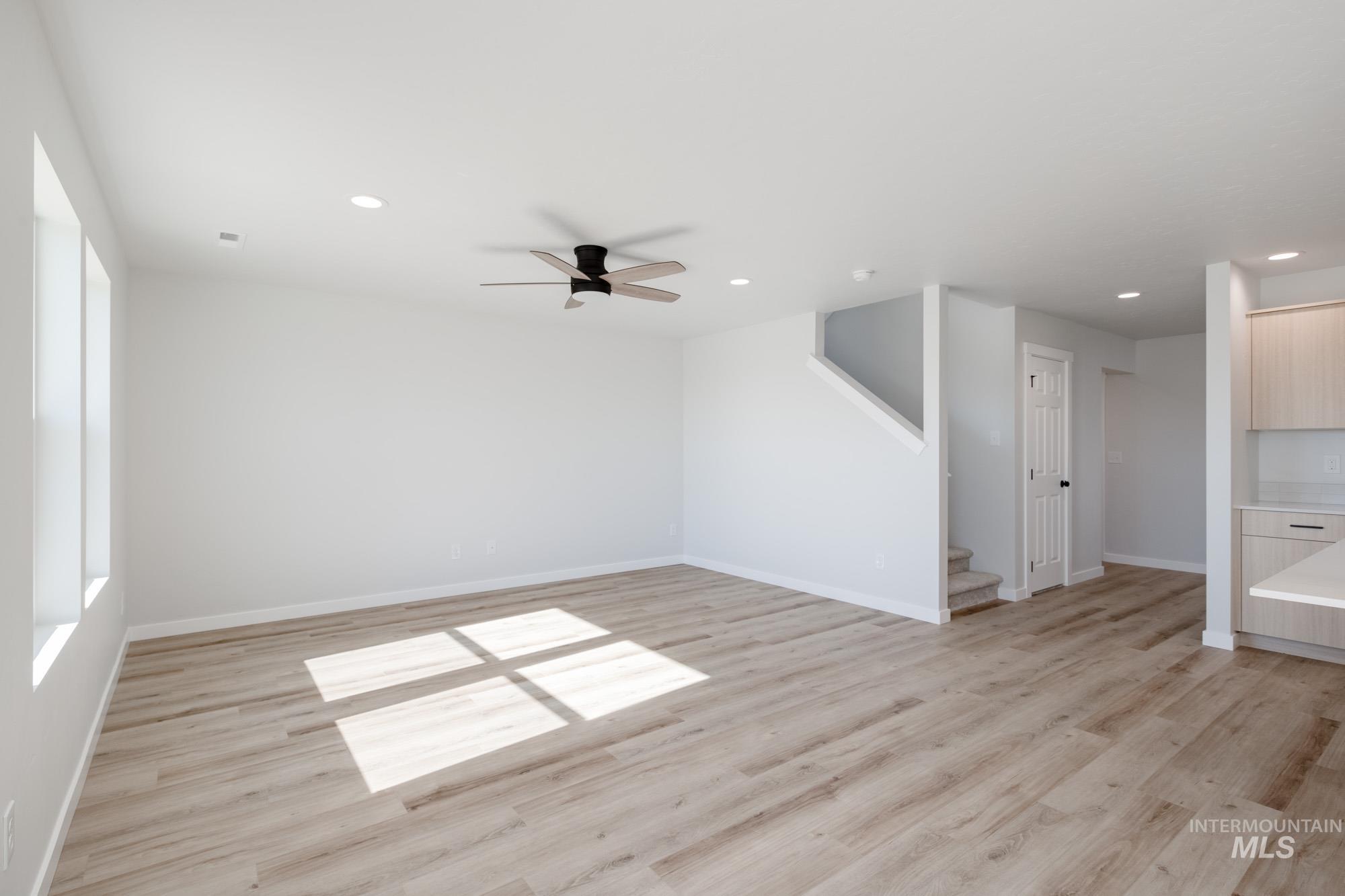 Unfurnished living room featuring light wood finished floors, a ceiling fan, recessed lighting, and stairway