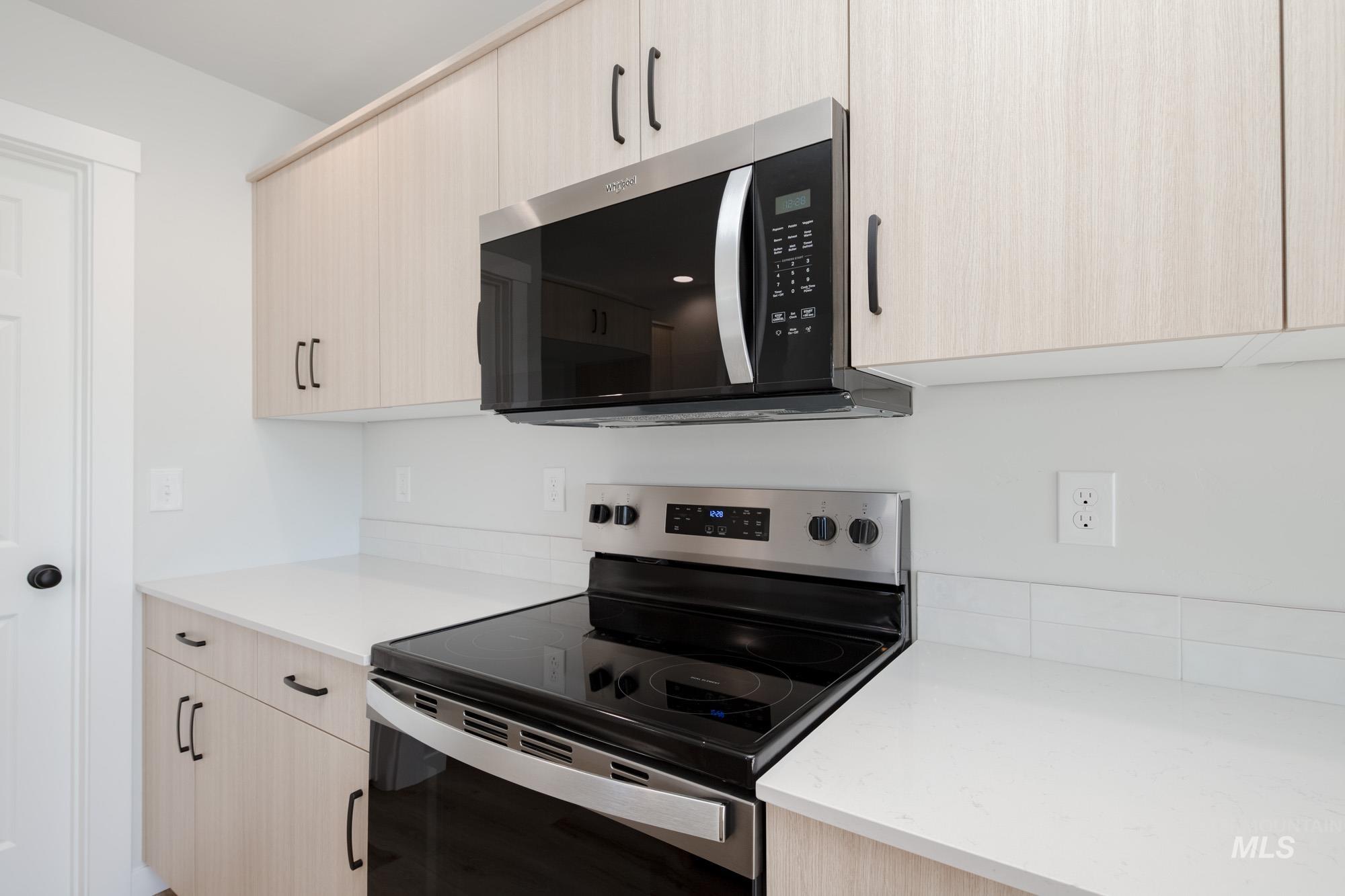 Kitchen featuring stainless steel appliances, light brown cabinets, light stone counters, and modern cabinets