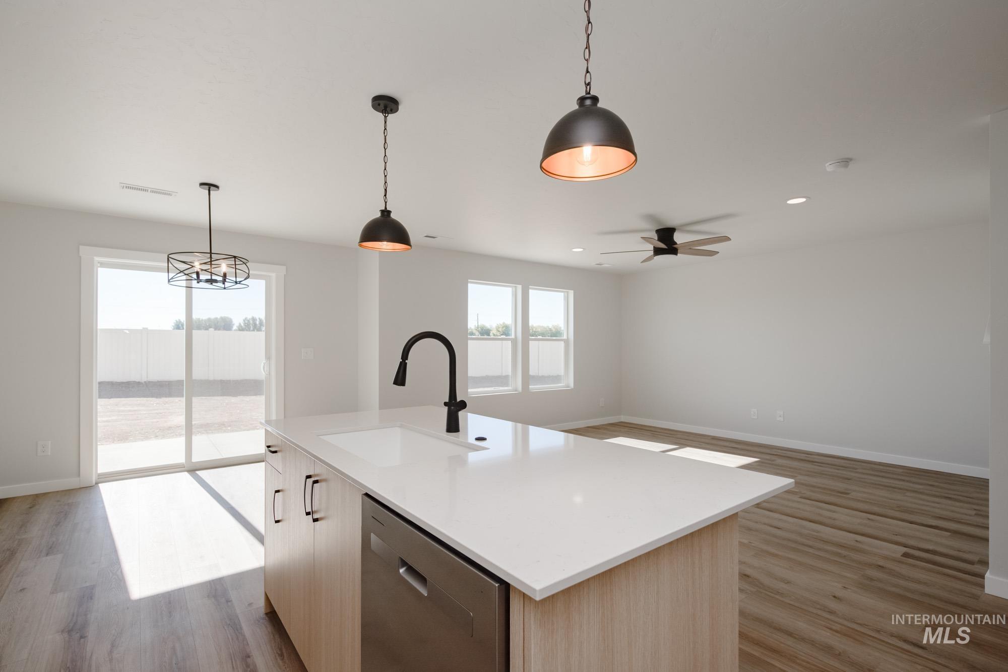 Kitchen featuring decorative light fixtures, stainless steel dishwasher, open floor plan, light wood finished floors, and a kitchen island with sink