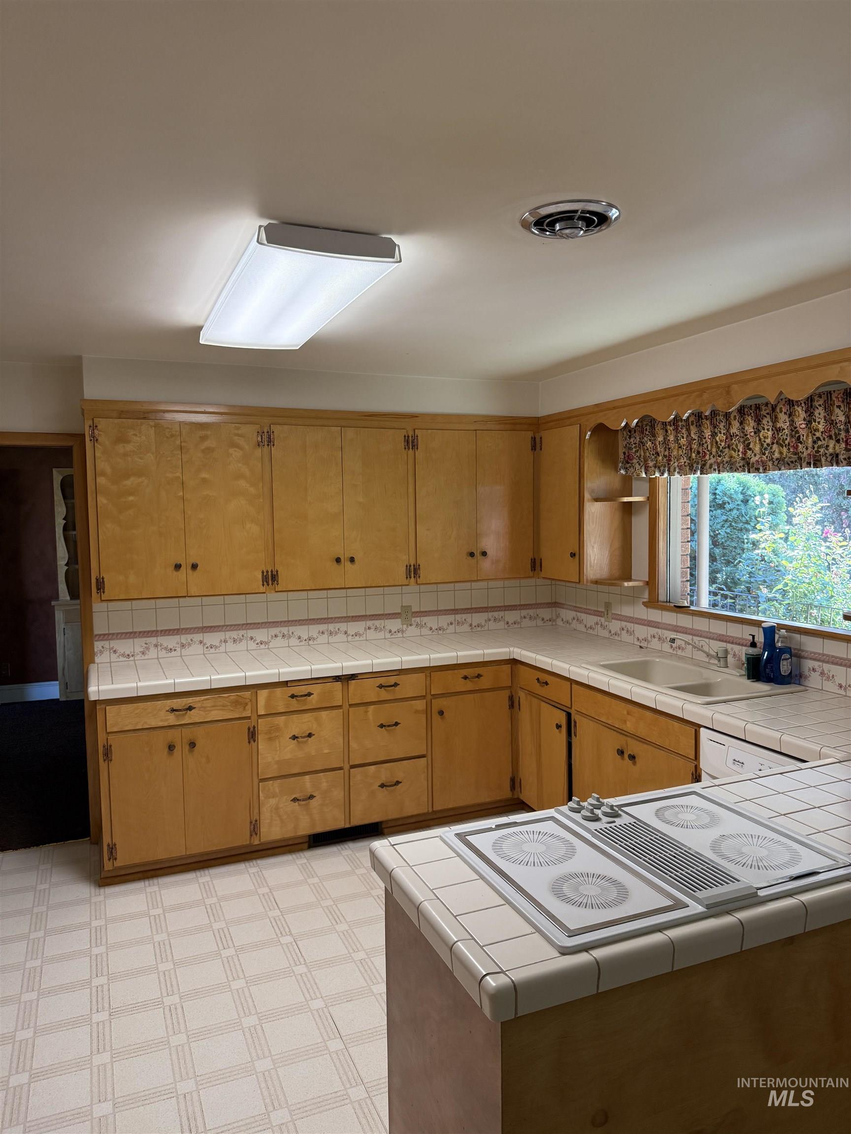 Kitchen featuring white electric stovetop, tile countertops, and brown cabinetry