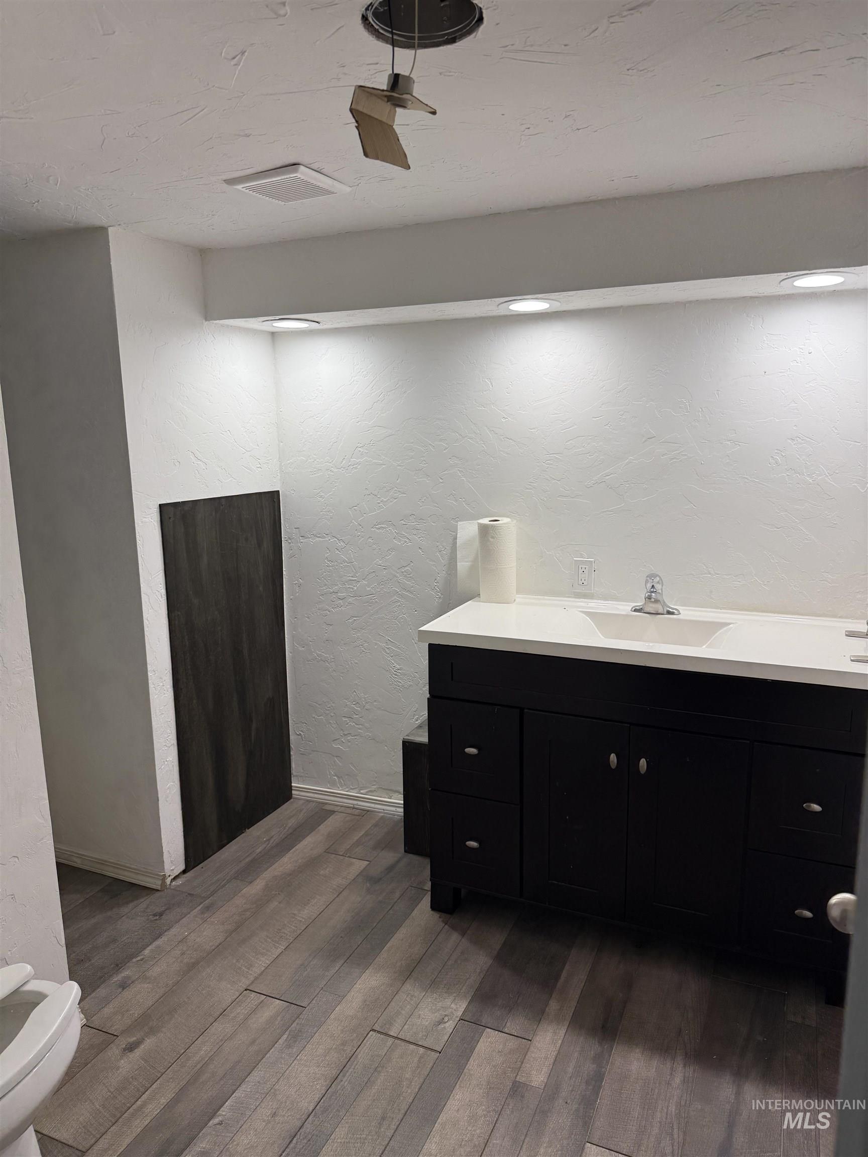 Bathroom with a textured wall, vanity, and dark wood-style floors