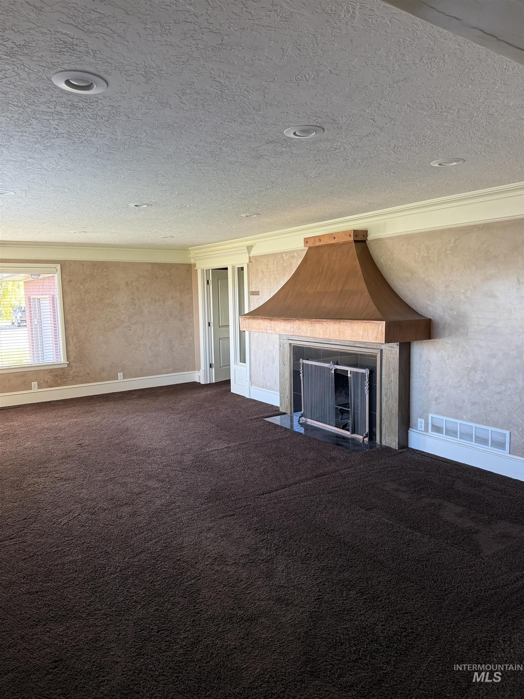 Unfurnished living room featuring a fireplace with flush hearth, dark carpet, a textured ceiling, and a textured wall
