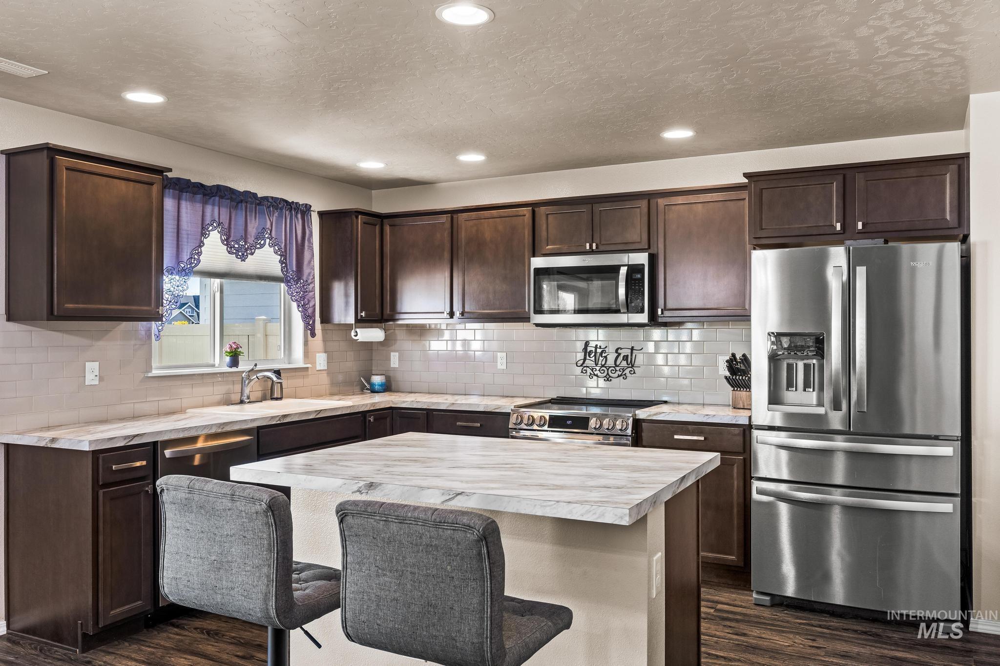 Kitchen with stainless steel appliances, light countertops, a kitchen bar, dark wood-style floors, and a textured ceiling