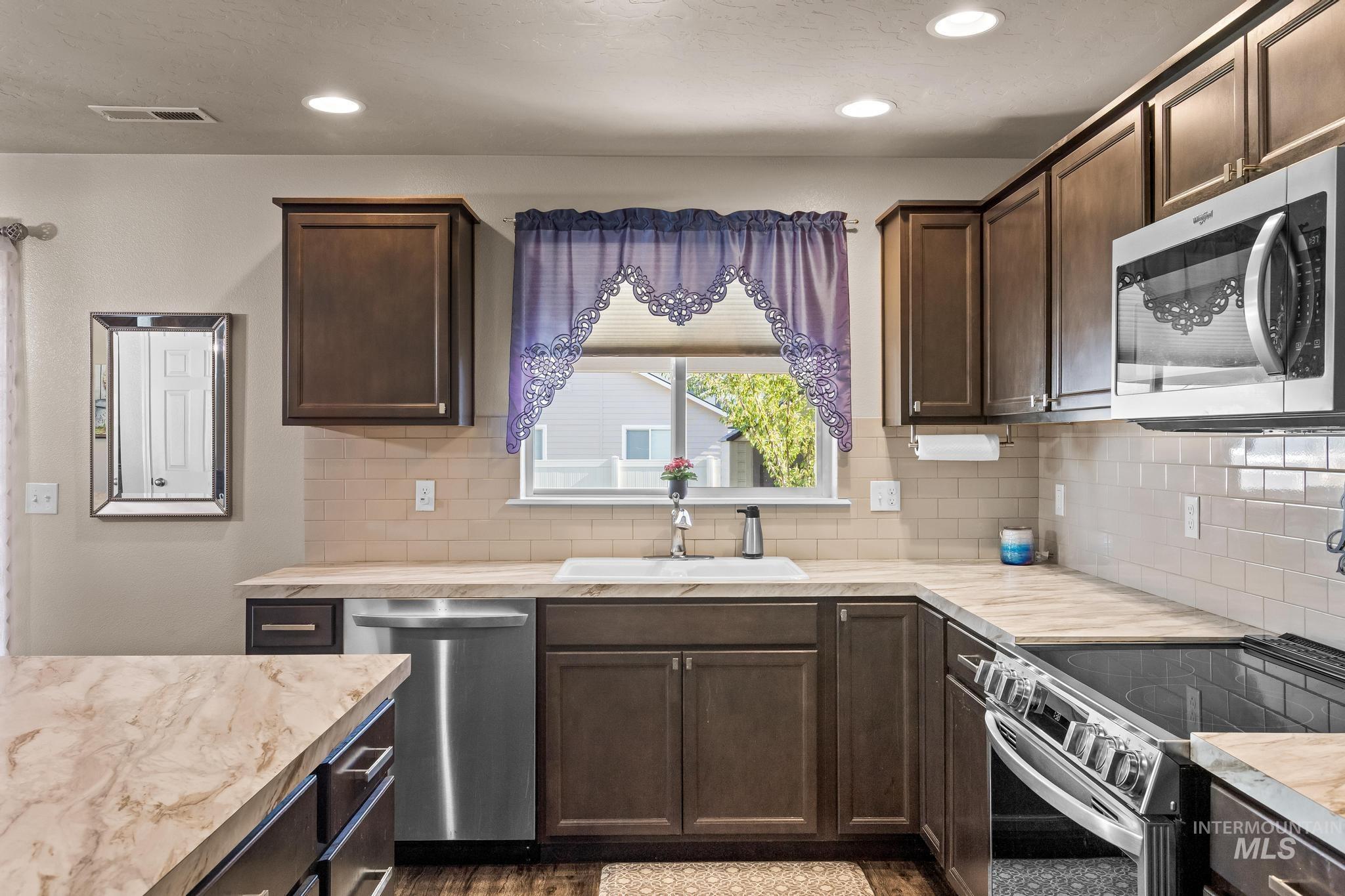 Kitchen featuring dark brown cabinets, appliances with stainless steel finishes, recessed lighting, and decorative backsplash