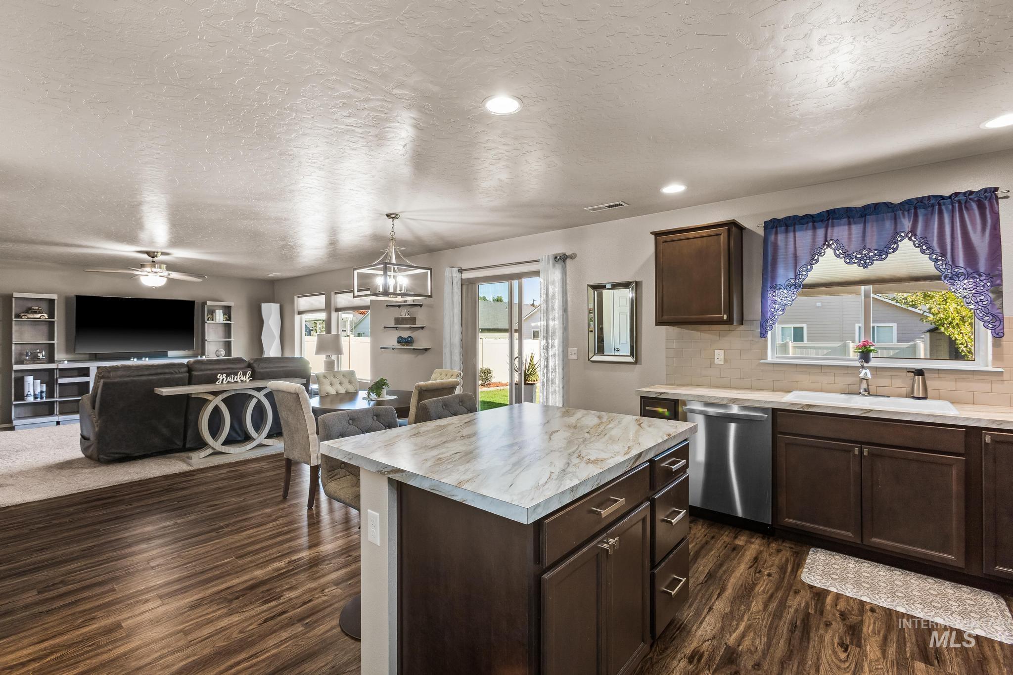 Kitchen featuring dark brown cabinets, light countertops, a textured ceiling, a kitchen island, and stainless steel dishwasher