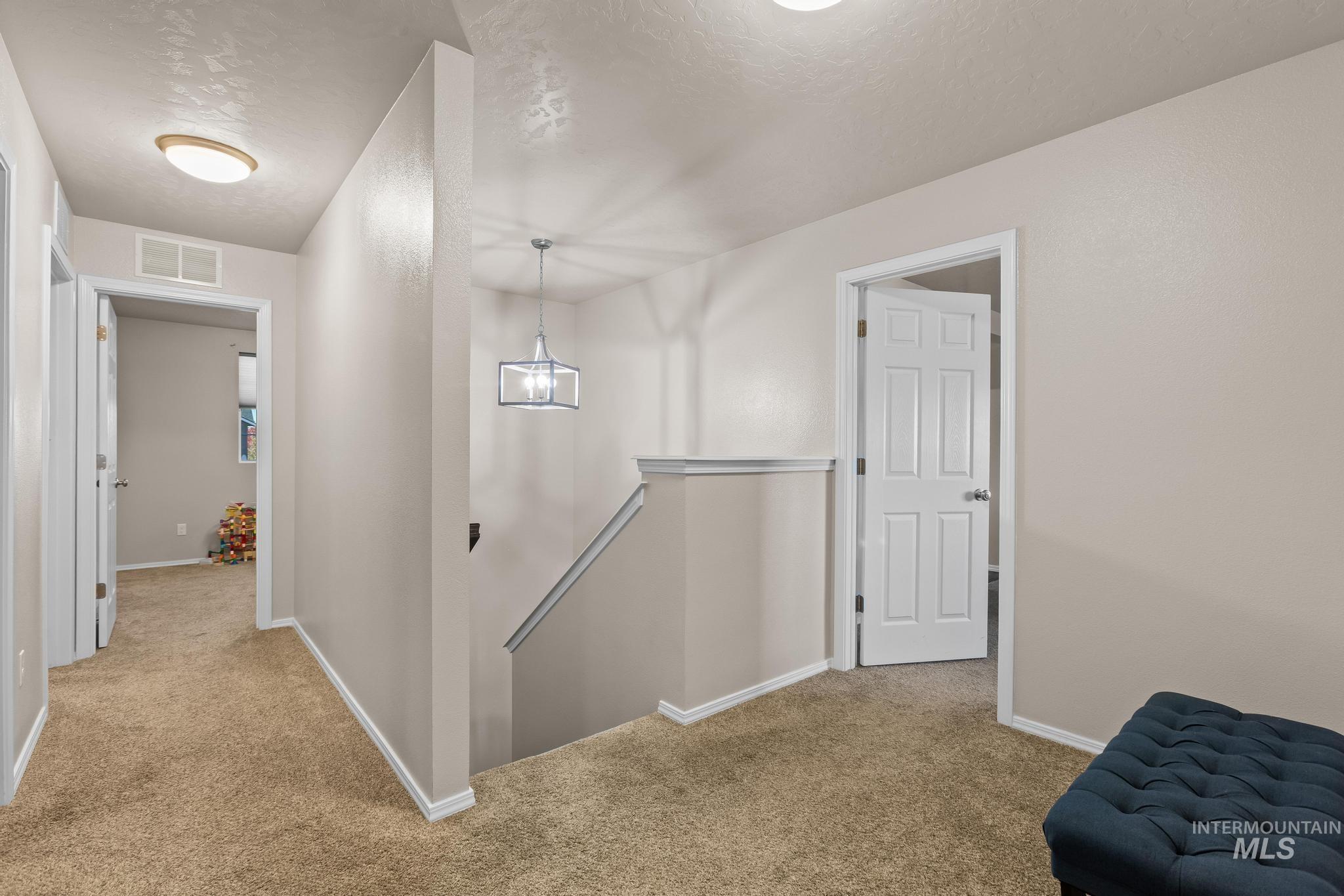 Corridor with an upstairs landing, light colored carpet, and a textured ceiling