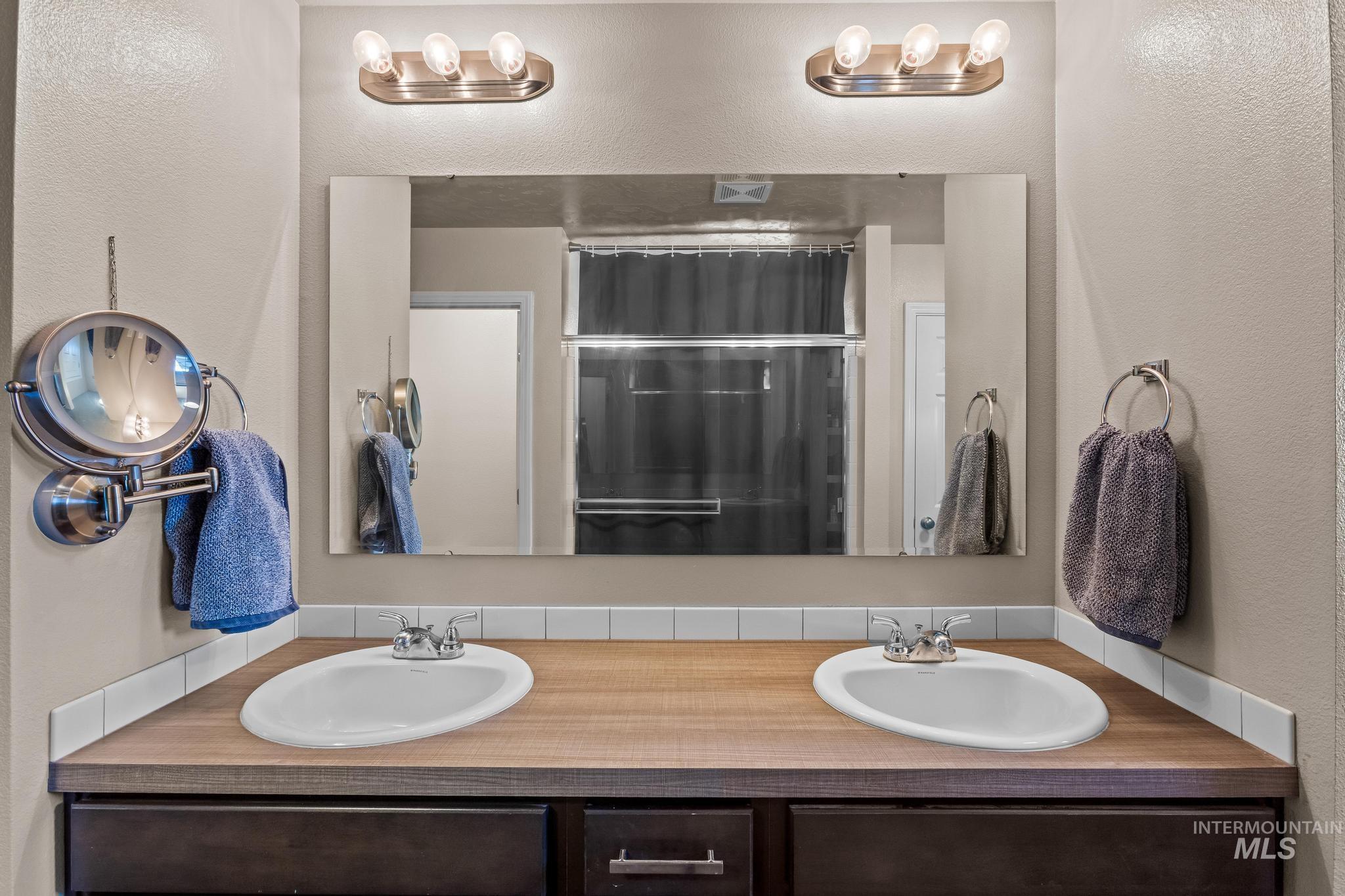 Bathroom featuring a textured wall, double vanity, and a shower with shower curtain