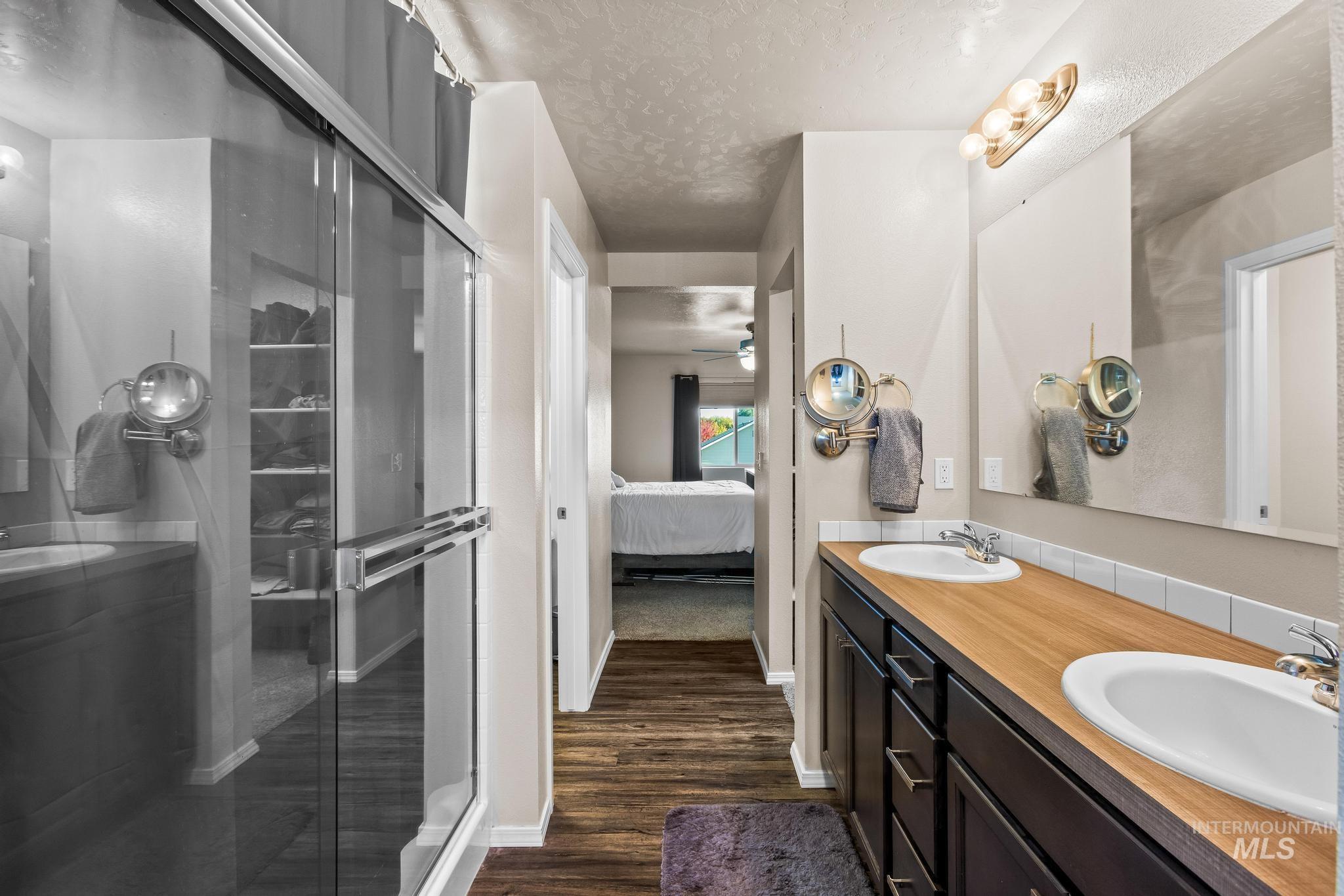 Ensuite bathroom featuring double vanity, a textured ceiling, dark wood finished floors, a shower stall, and ceiling fan