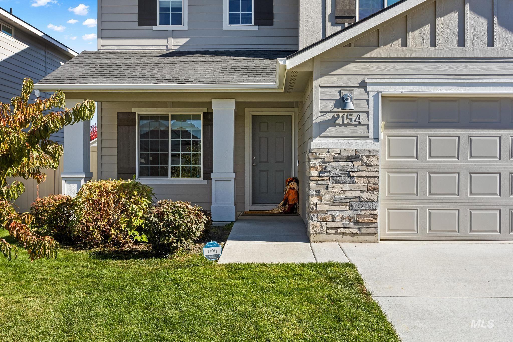 Doorway to property featuring a garage, a lawn, roof with shingles, and stone siding