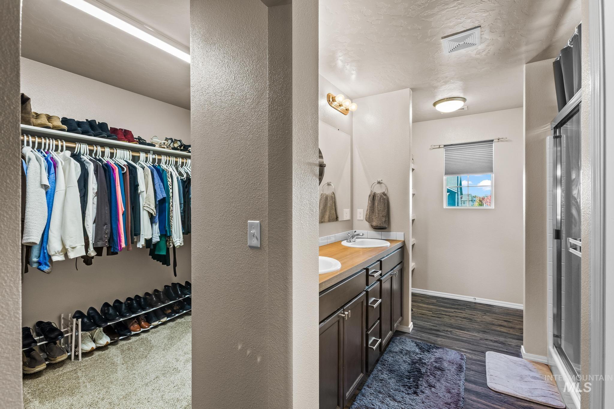 Bathroom with double vanity, a spacious closet, dark wood-style flooring, a shower stall, and a textured ceiling