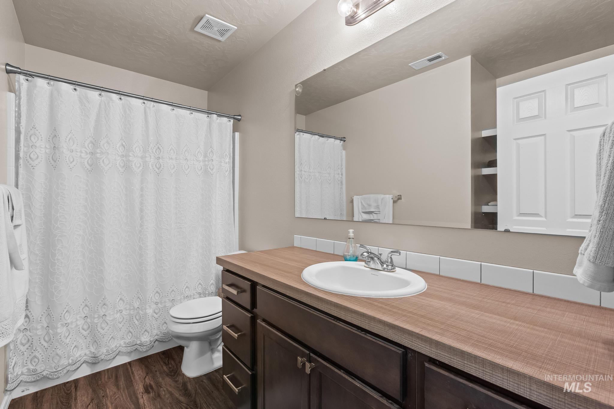 Bathroom with a textured ceiling, vanity, dark wood-type flooring, and shower / tub combo with curtain