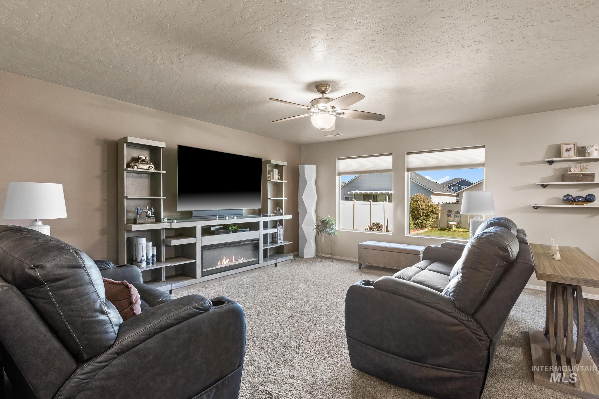 Living room with carpet floors, a textured ceiling, a ceiling fan, and a glass covered fireplace