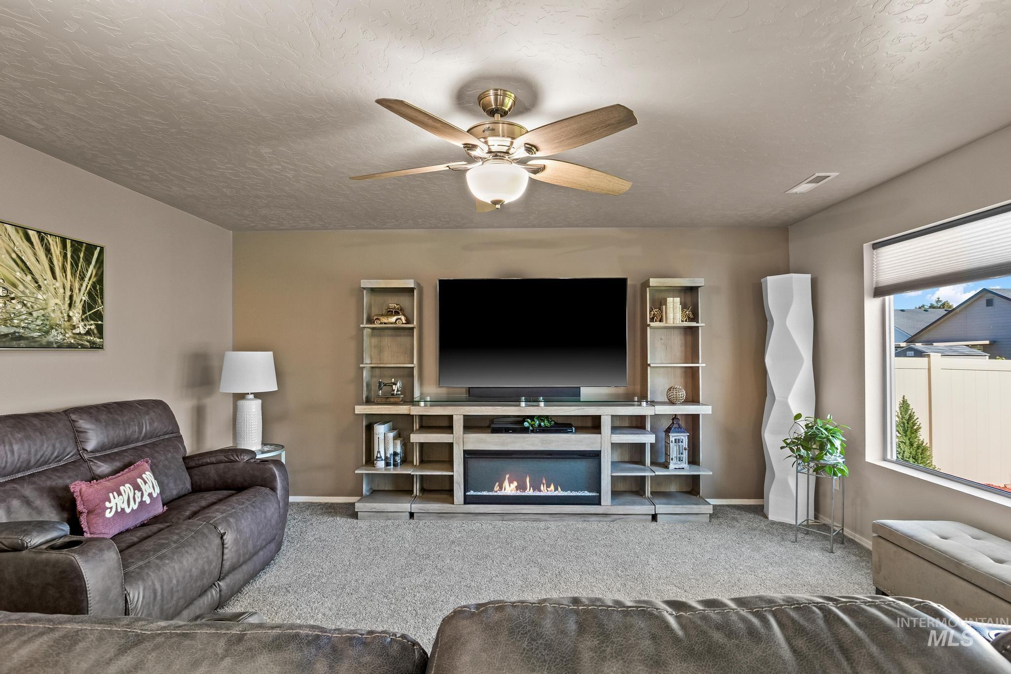 Carpeted living room with a ceiling fan, a textured ceiling, and a lit fireplace