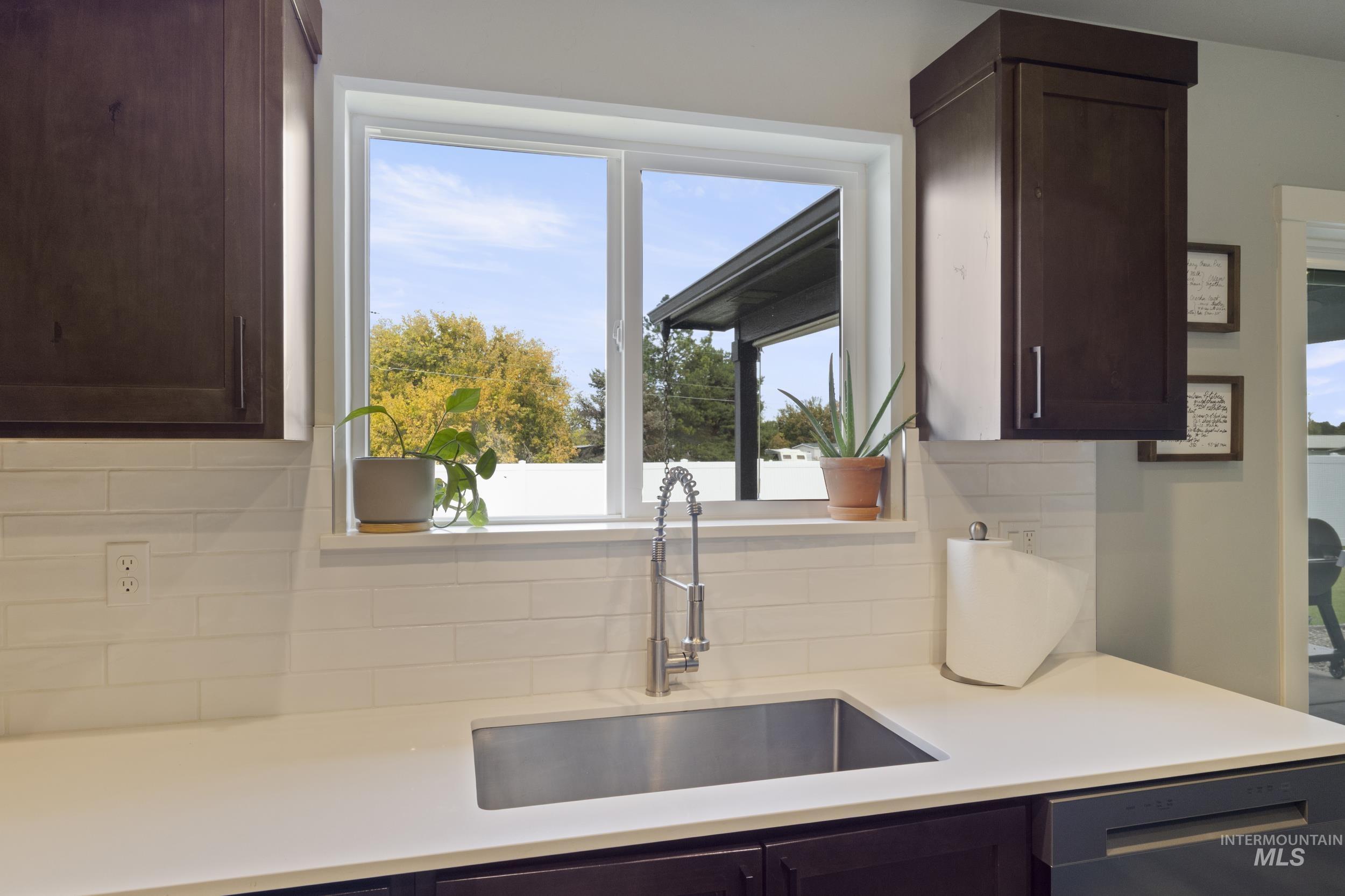 Kitchen featuring dark brown cabinetry, decorative backsplash, stainless steel dishwasher, and light stone counters