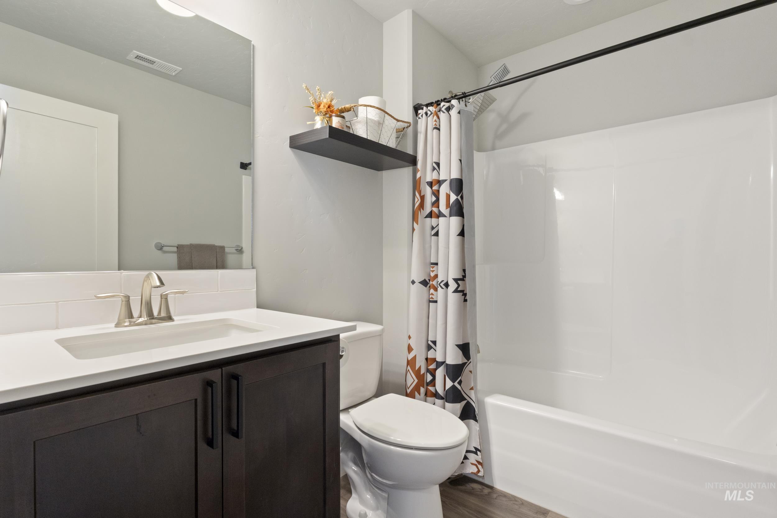 Full bath with vanity, shower / bathtub combination with curtain, and dark wood-style floors