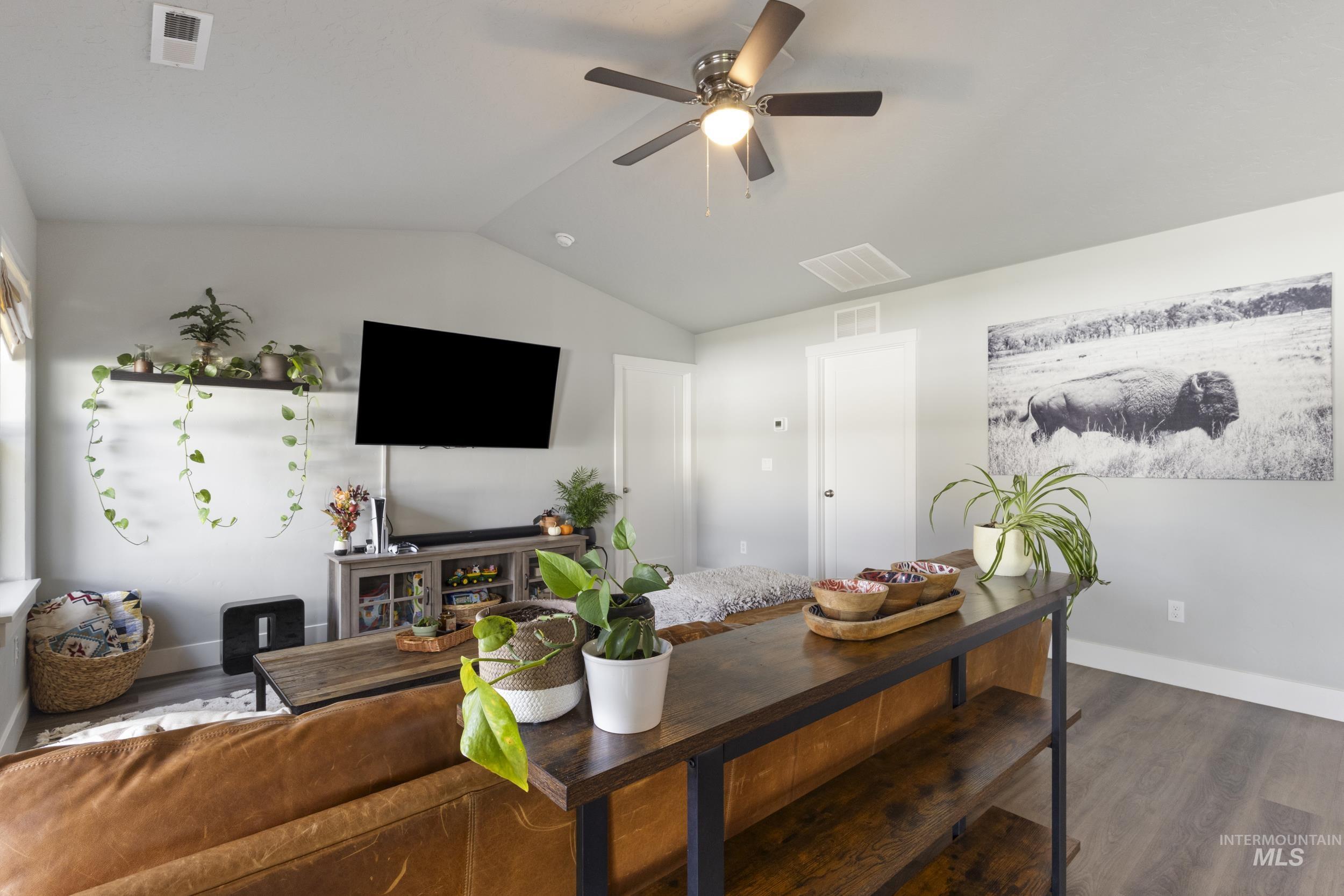 Living room with dark wood finished floors, vaulted ceiling, and a ceiling fan