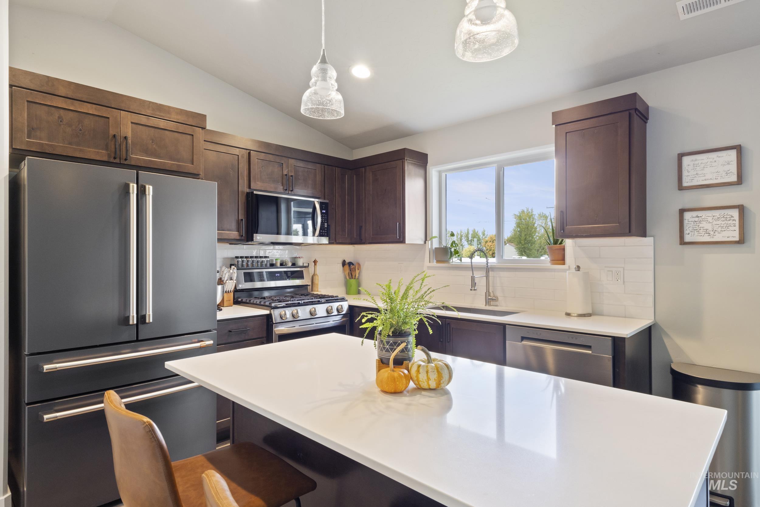 Kitchen featuring appliances with stainless steel finishes, dark brown cabinets, a breakfast bar area, a kitchen island, and tasteful backsplash