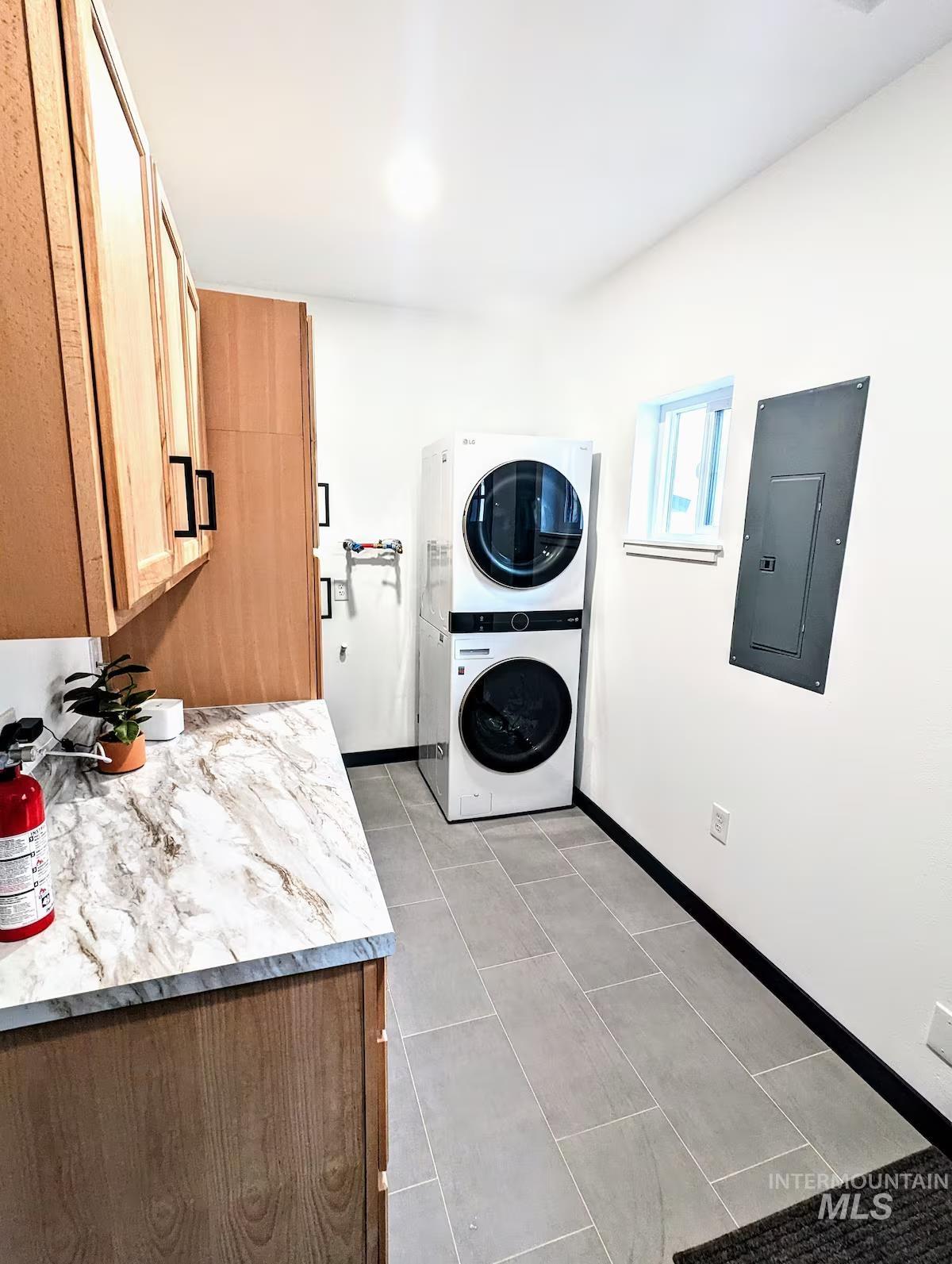 Laundry area with electric panel, stacked washer / drying machine, Water Softener Hook-up, light tile patterned floors, and cabinet space