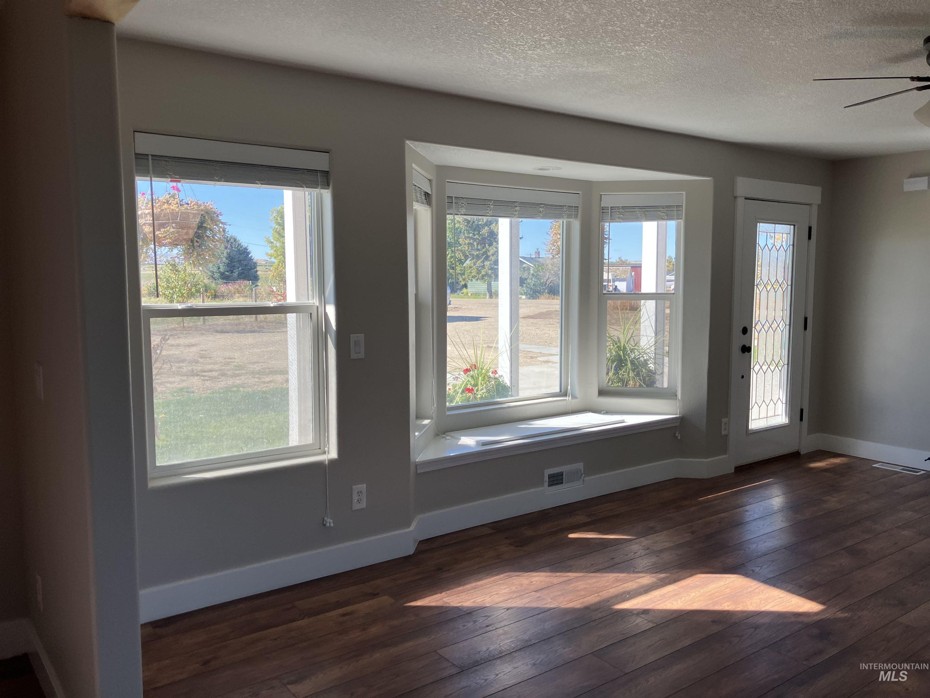 Entrance foyer with plenty of natural light, a textured ceiling, dark wood-type flooring, and ceiling fan