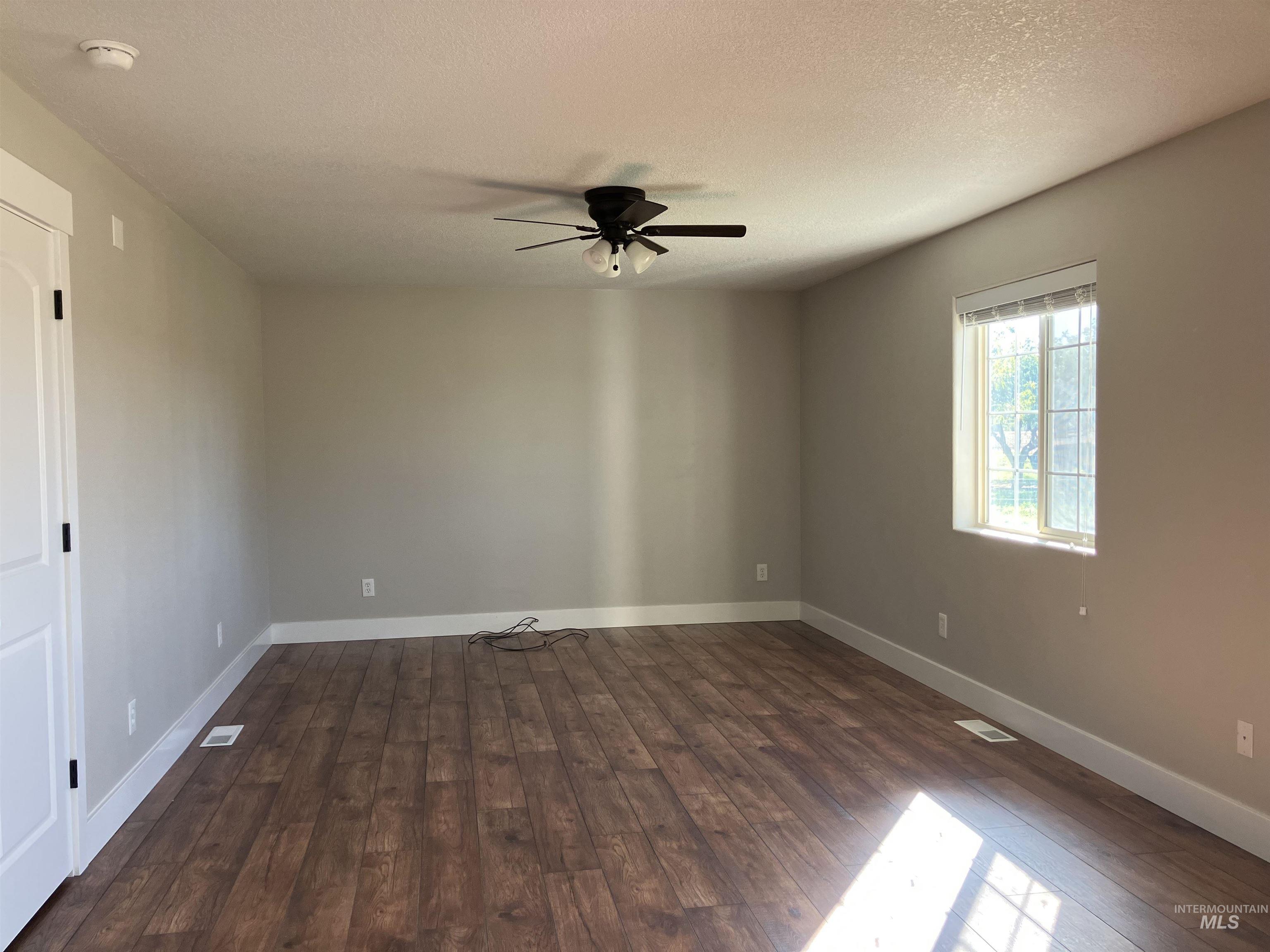 Spare room with a textured ceiling, dark wood-style floors, and a ceiling fan