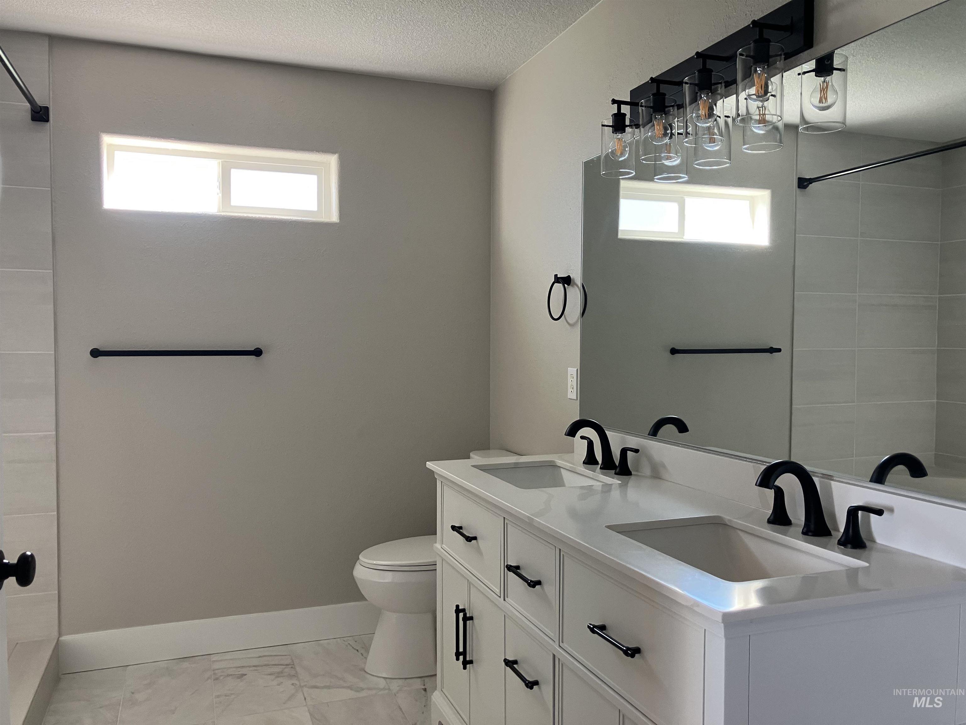 Bathroom with double vanity, light marble finish flooring, a textured ceiling, and tiled shower / bath combo