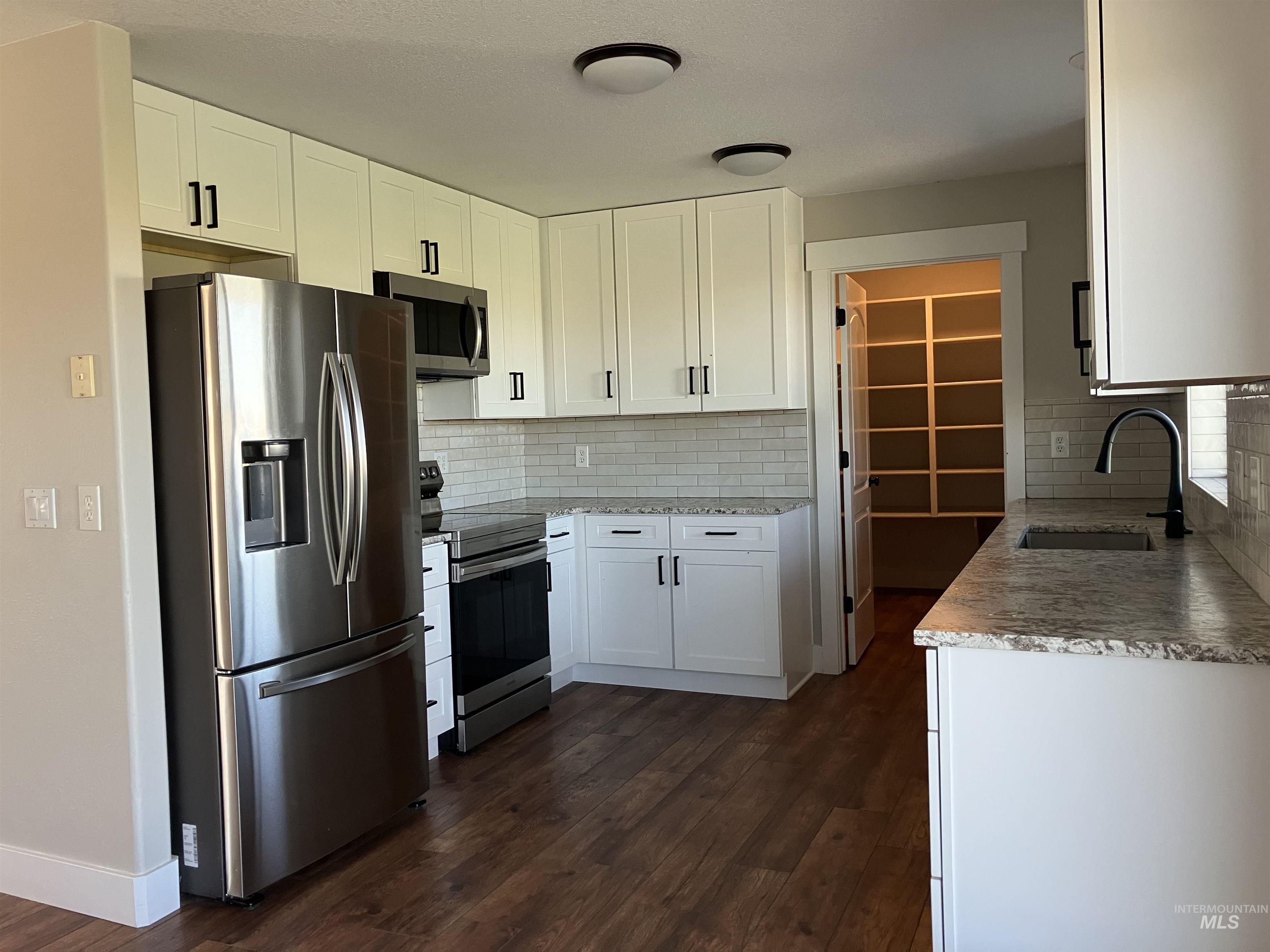 Kitchen featuring stainless steel appliances, white cabinets, dark wood-style floors, and backsplash