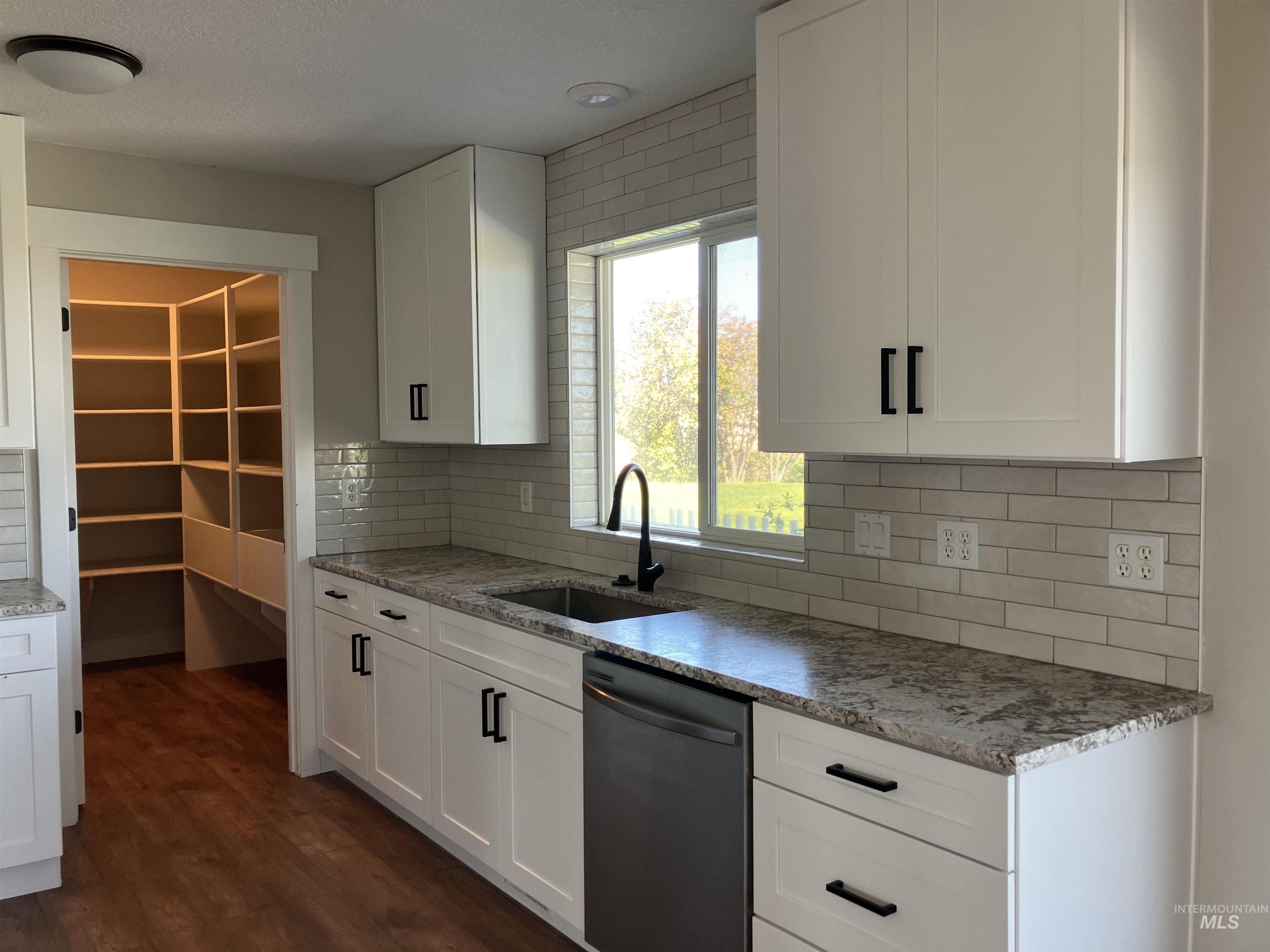 Kitchen featuring stainless steel dishwasher, light stone counters, white cabinets, tasteful backsplash, and dark wood-style floors