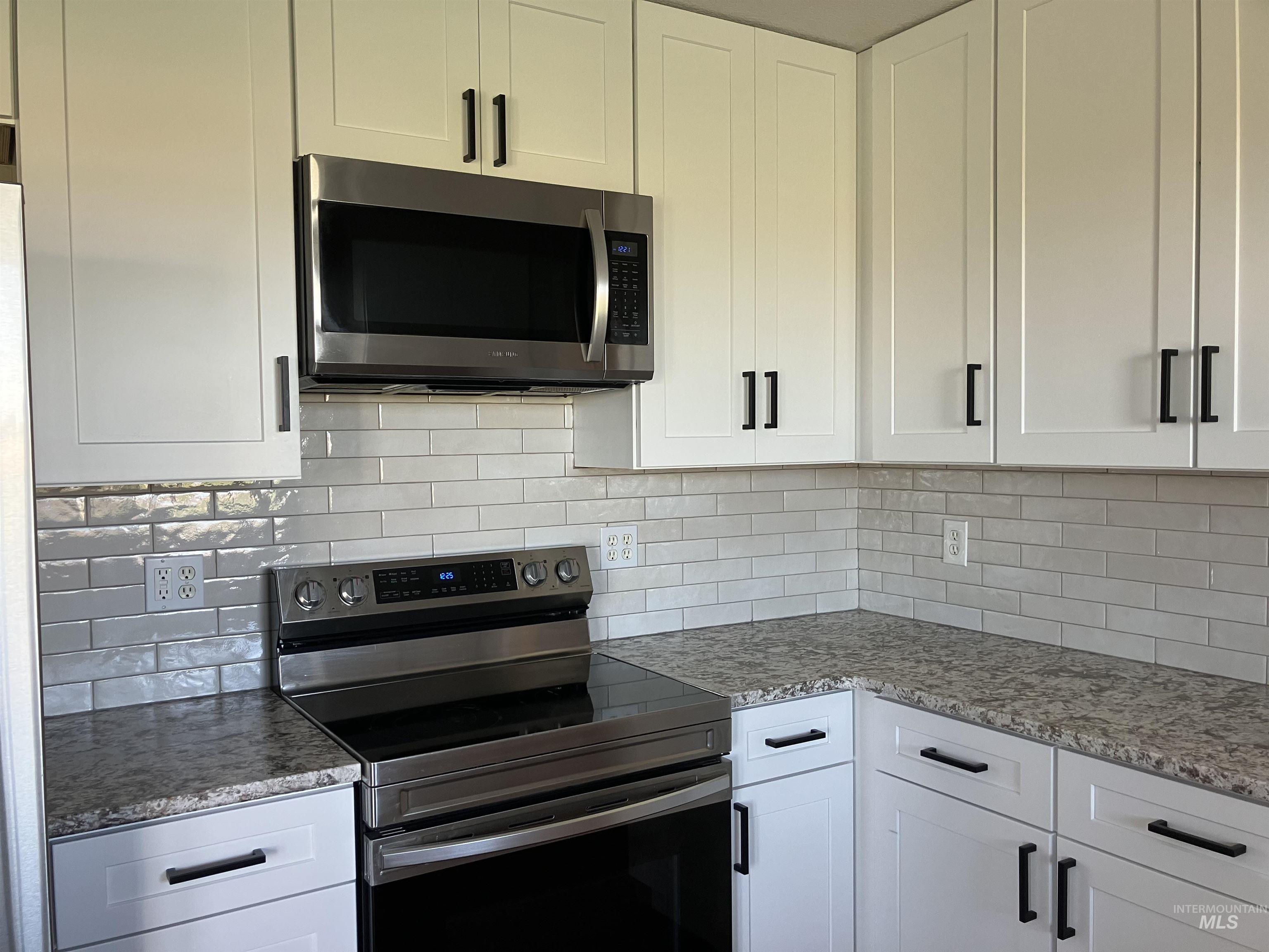 Kitchen with stainless steel appliances, white cabinets, and light stone counters