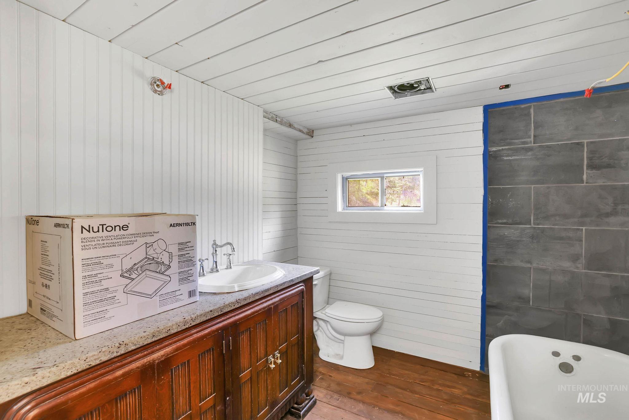 Full bathroom featuring a freestanding tub, wood finished floors, vanity, and wooden walls