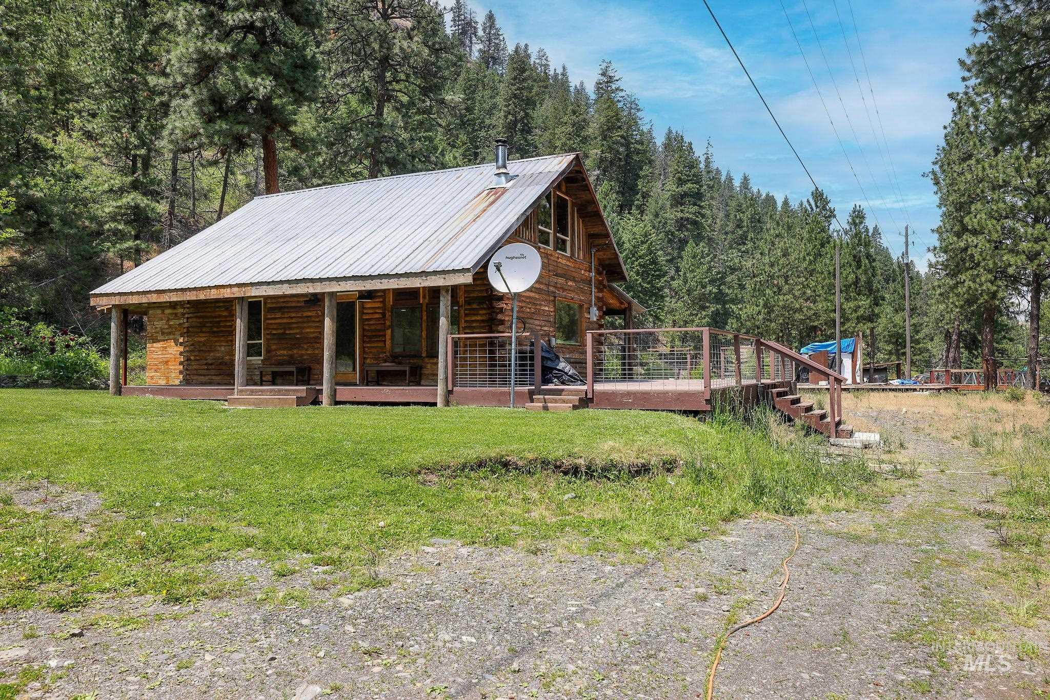 View of front of house with log siding, a metal roof, covered porch, a front yard, and a forest view