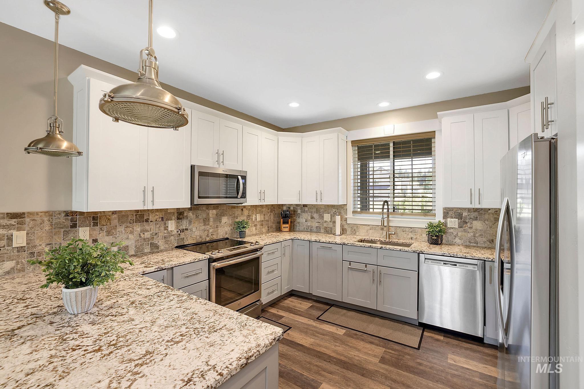 Kitchen featuring stainless steel appliances, hanging light fixtures, dark wood finished floors, light stone counters, and recessed lighting