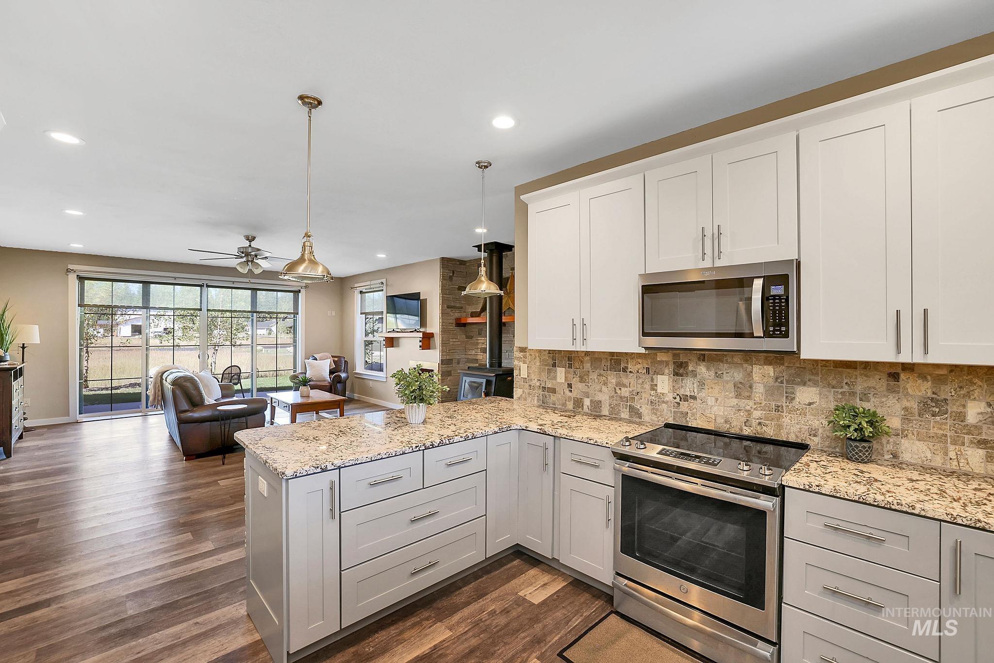 Kitchen with appliances with stainless steel finishes, hanging light fixtures, light stone countertops, open floor plan, and backsplash