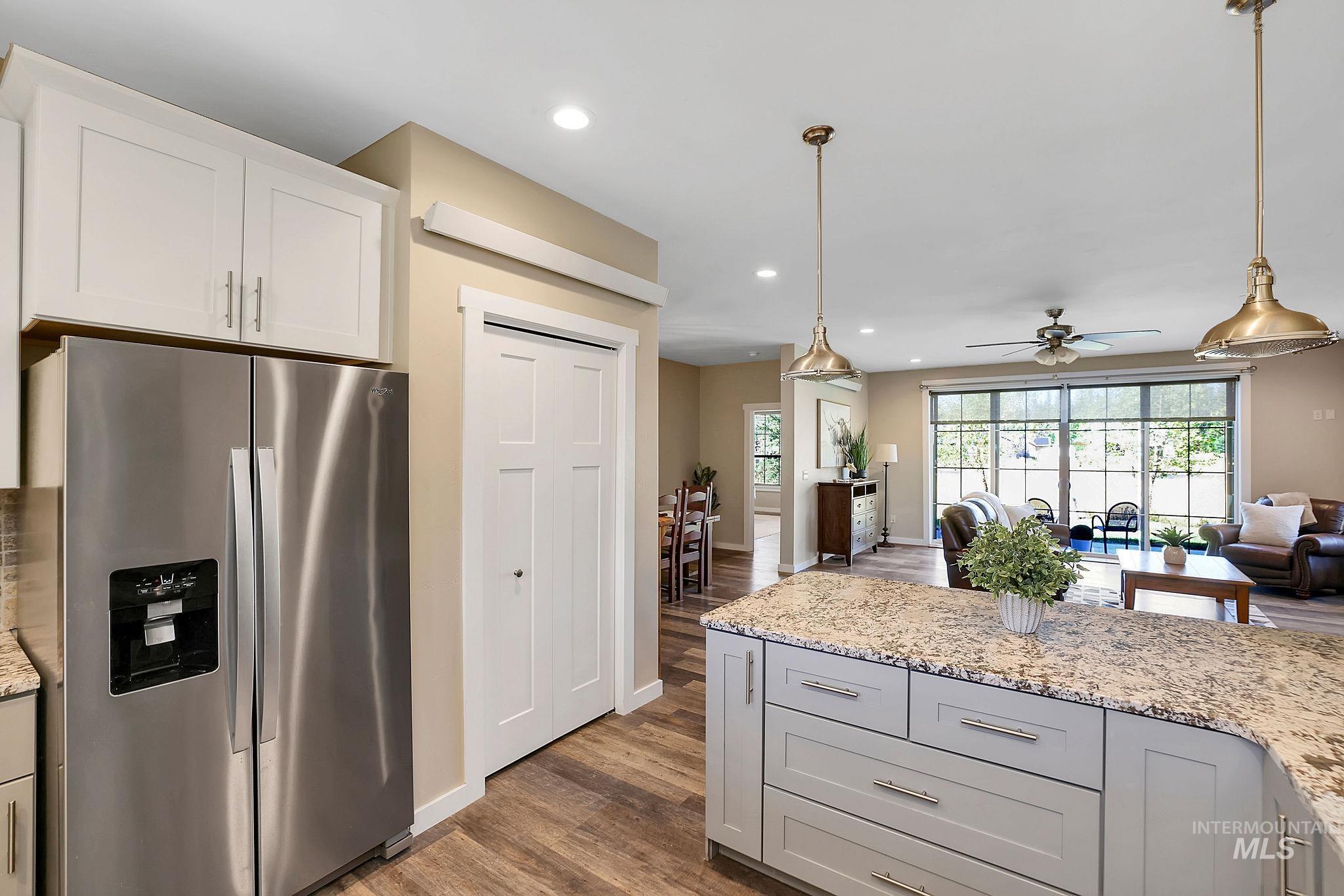 Kitchen with stainless steel fridge, recessed lighting, dark wood finished floors, light stone countertops, and hanging light fixtures