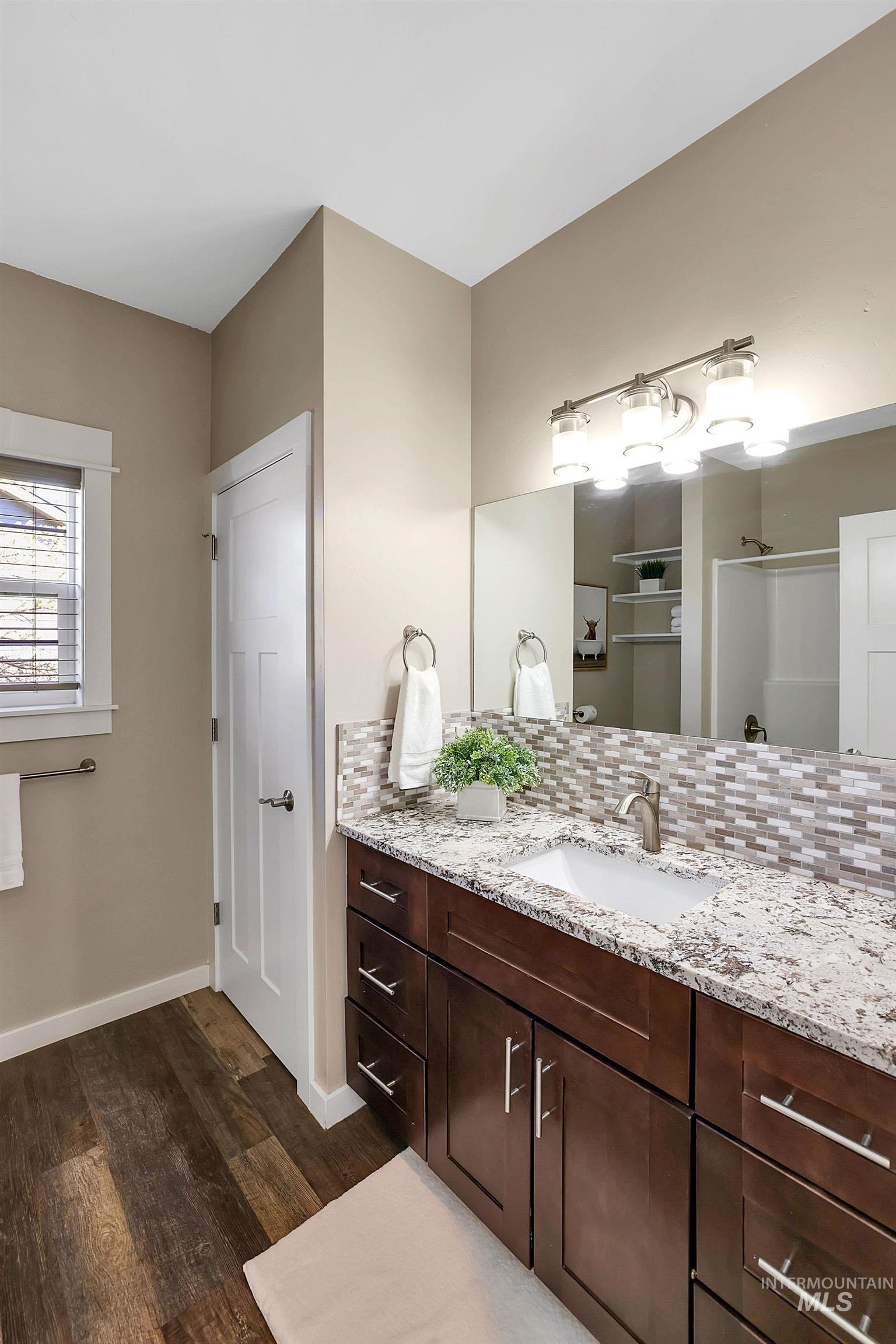Bathroom featuring vanity, dark wood finished floors, decorative backsplash, and a shower