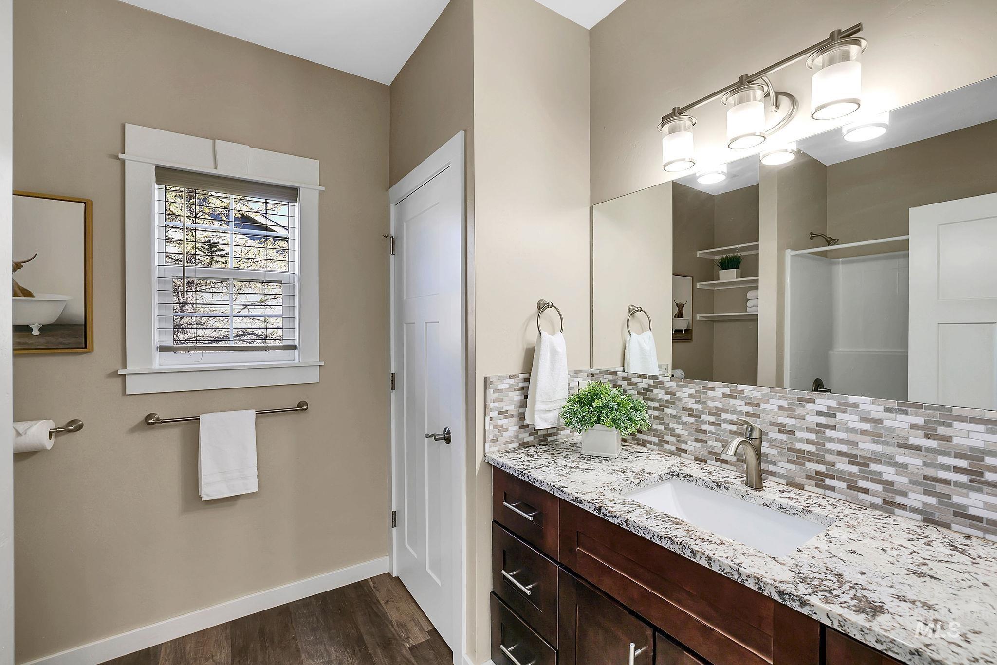 Bathroom with backsplash, vanity, dark wood-type flooring, and a shower