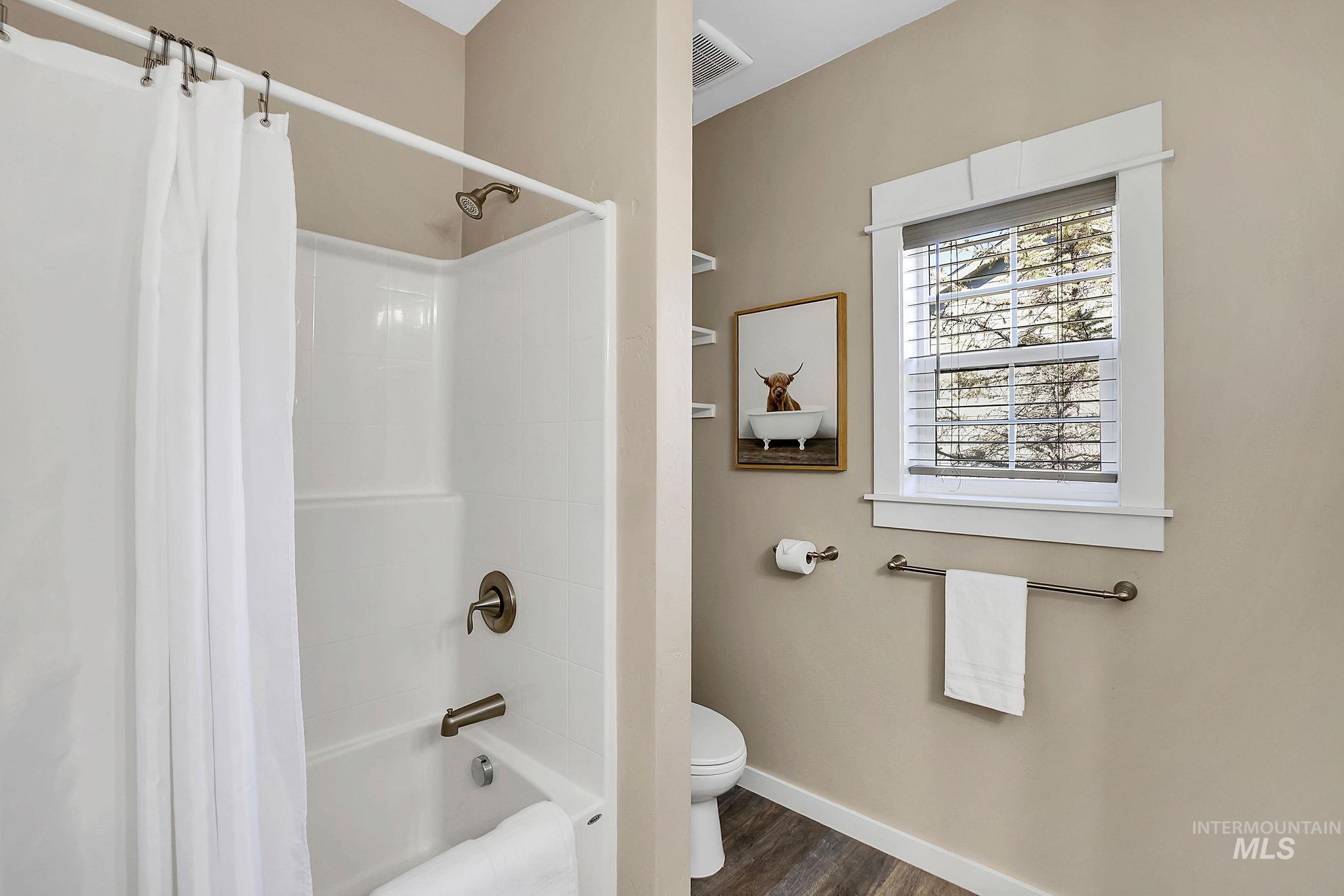 Full bath featuring shower / bath combination with curtain and dark wood-style floors