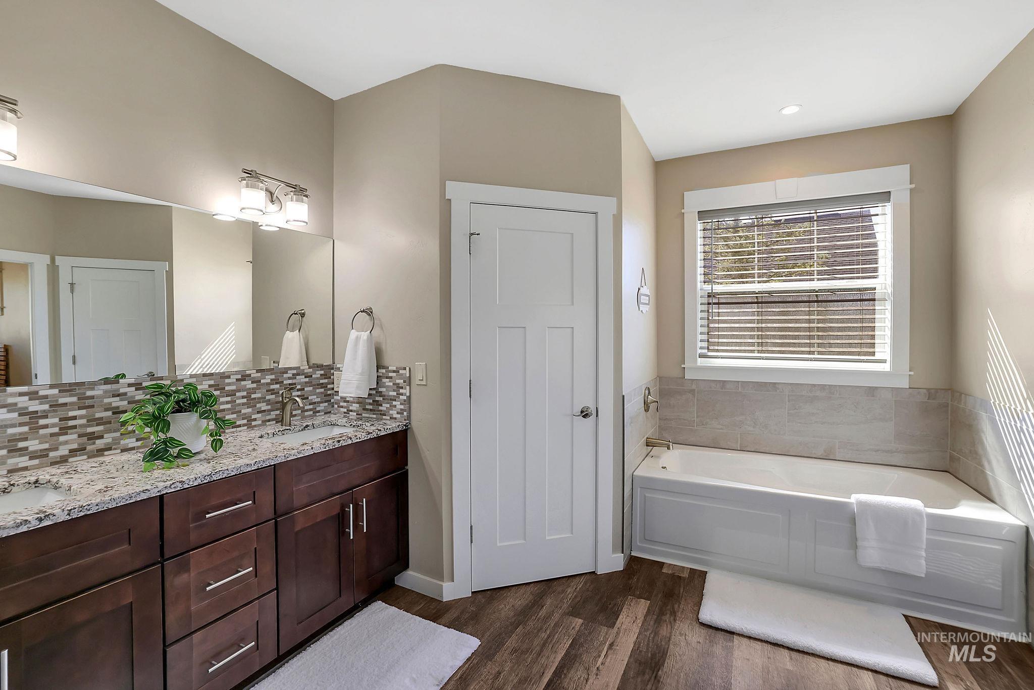 Bathroom featuring a garden tub, double vanity, dark wood finished floors, and tasteful backsplash
