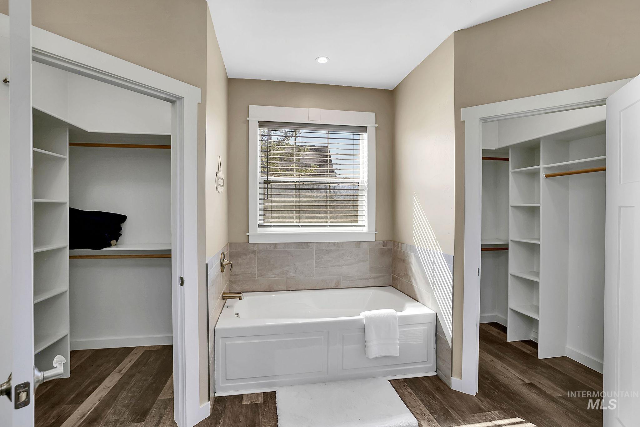 Bathroom featuring a spacious closet, a garden tub, and dark wood-style floors