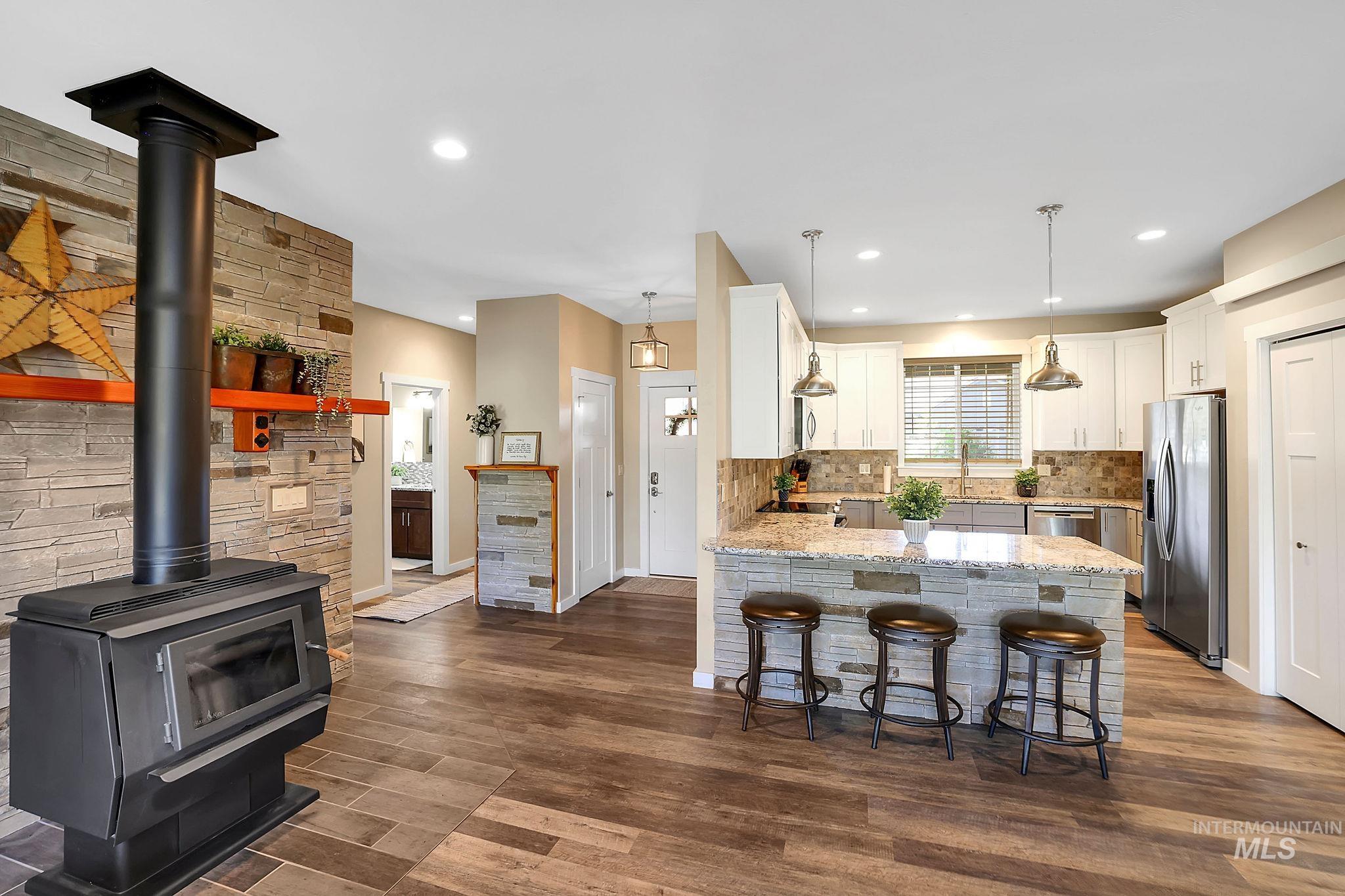 Kitchen featuring a peninsula, light stone counters, a kitchen bar, a wood stove, and pendant lighting