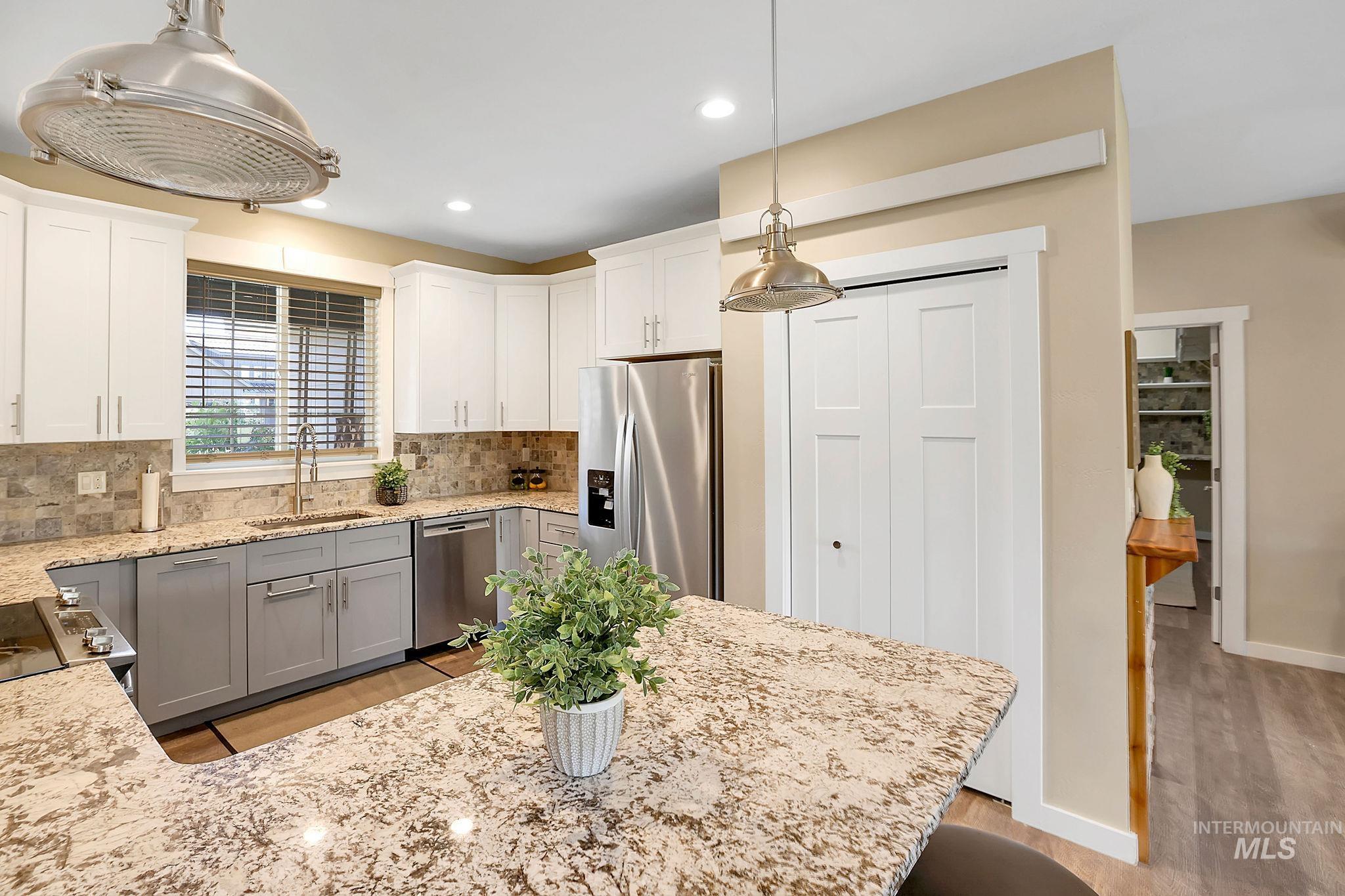 Kitchen with appliances with stainless steel finishes, pendant lighting, light wood-style floors, light stone counters, and decorative backsplash