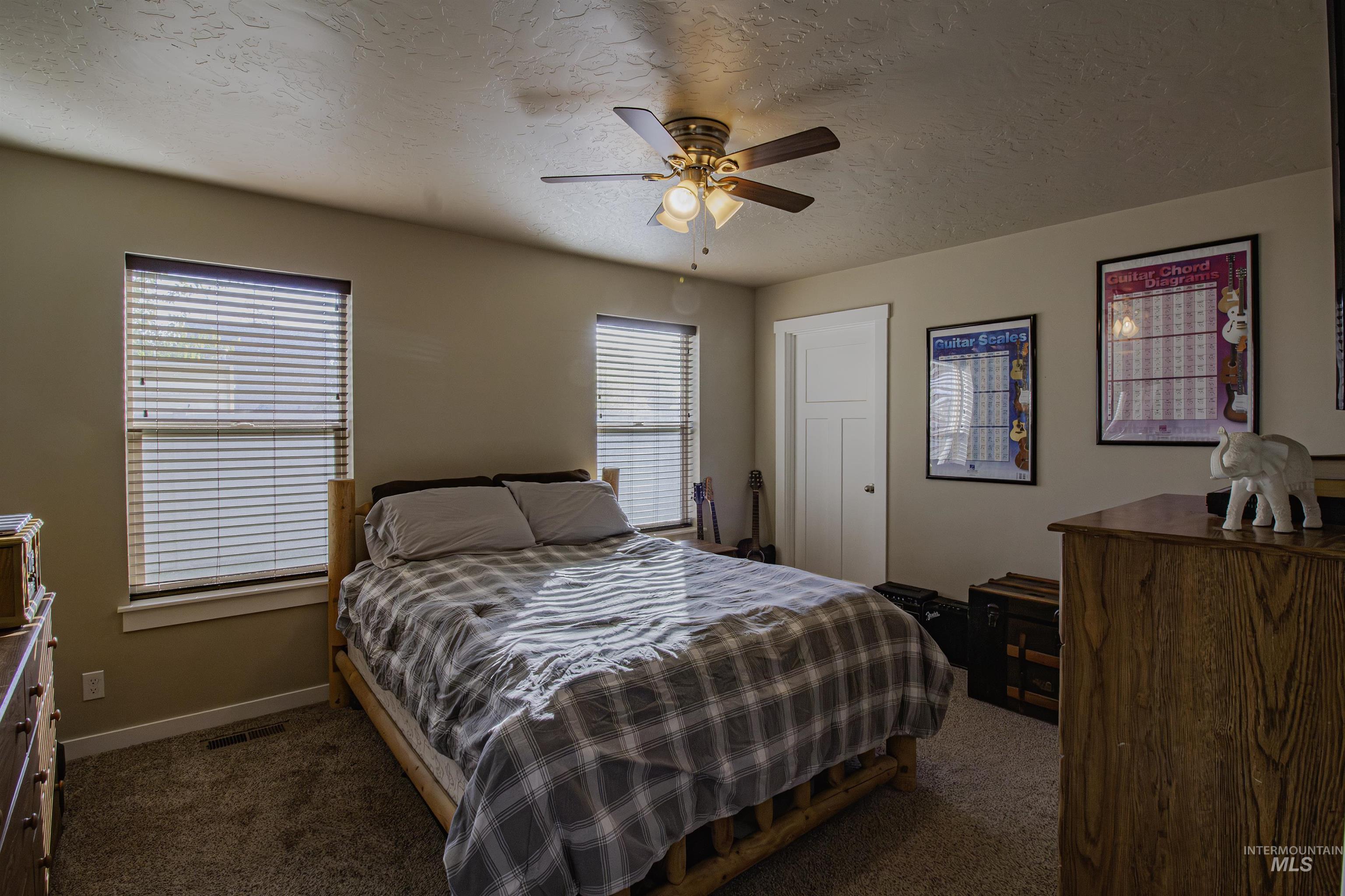 Bedroom with a textured ceiling, dark carpet, and ceiling fan