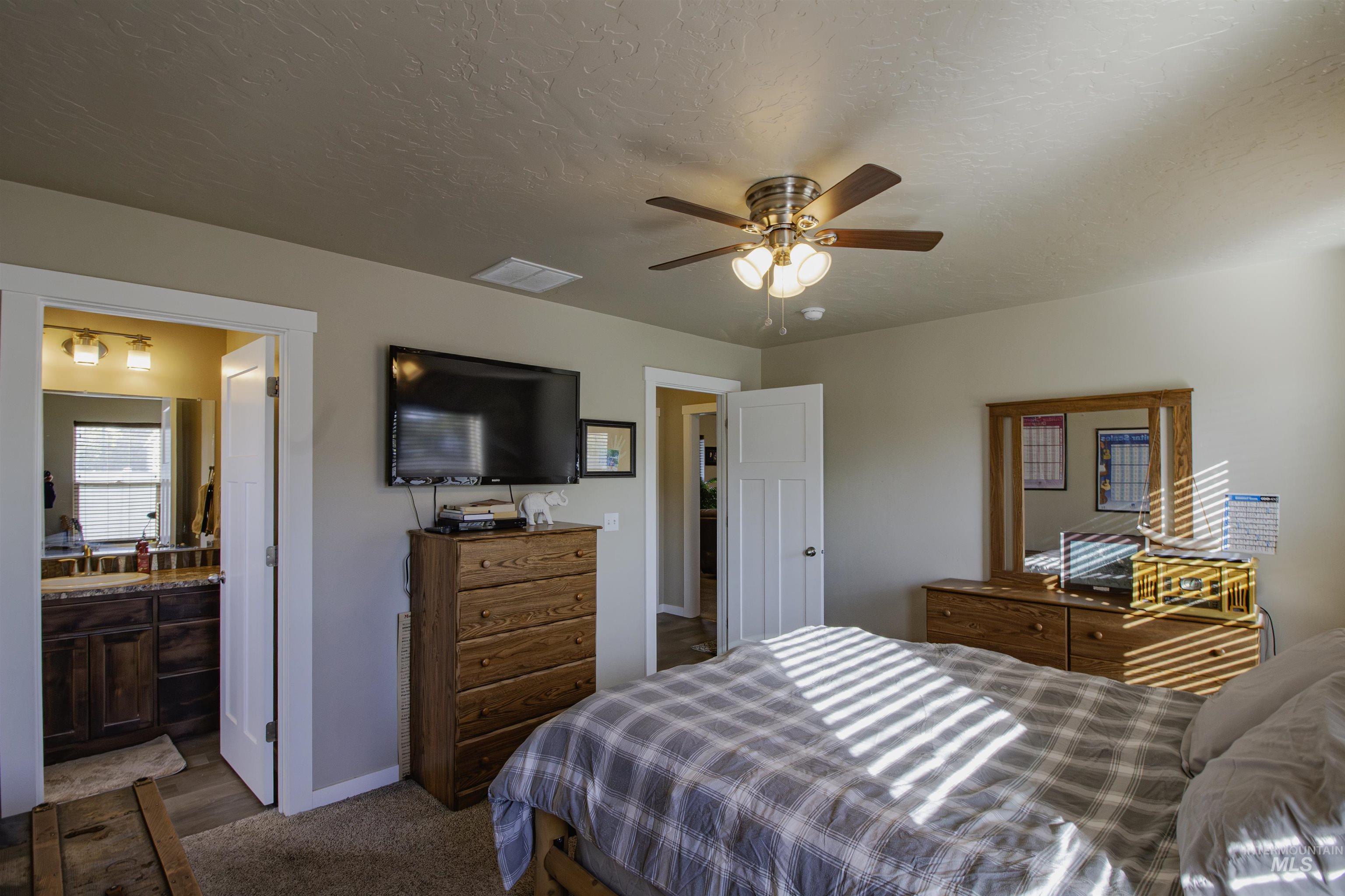 Bedroom featuring dark colored carpet, a textured ceiling, ceiling fan, and connected bathroom