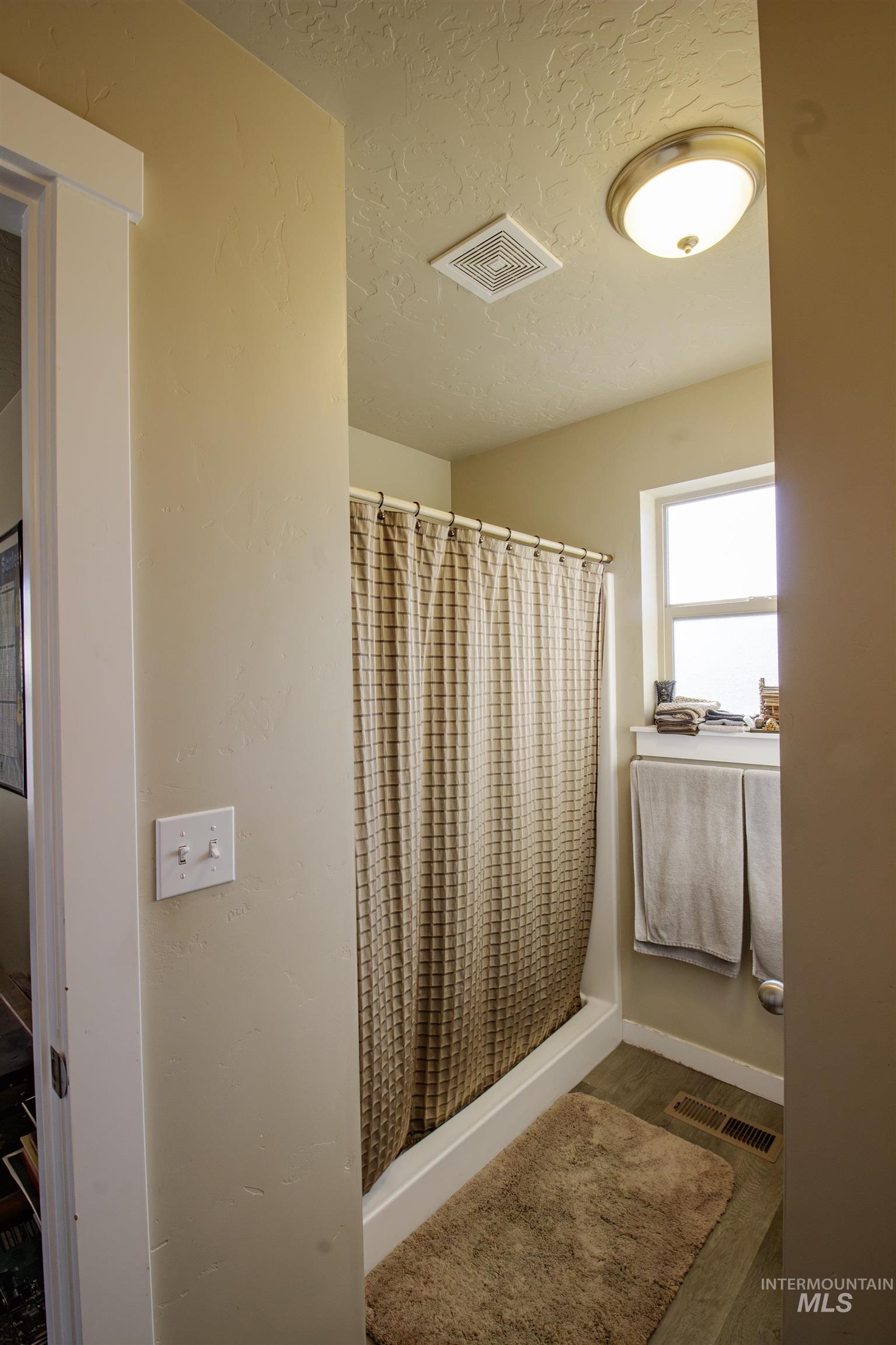 Bathroom featuring a walk-in shower, a textured ceiling, and dark wood-type flooring